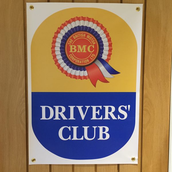 BMC DRIVERS' CLUB BANNER. A white banner with brass eyelets. Printed on the banner is the BMC rosette and Drivers' Club in white uppercase lettering on a half yellow, half blue background.