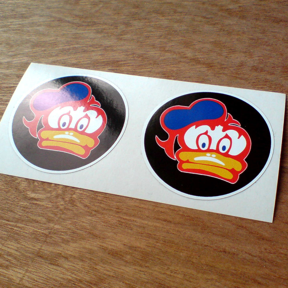 BARRY SHEENE DUCK STICKERS BLACK. A cartoon character duck with a white face, blue eyes and a yellow bill wearing a blue sailor cap; all outlined in red on a black circular sticker.