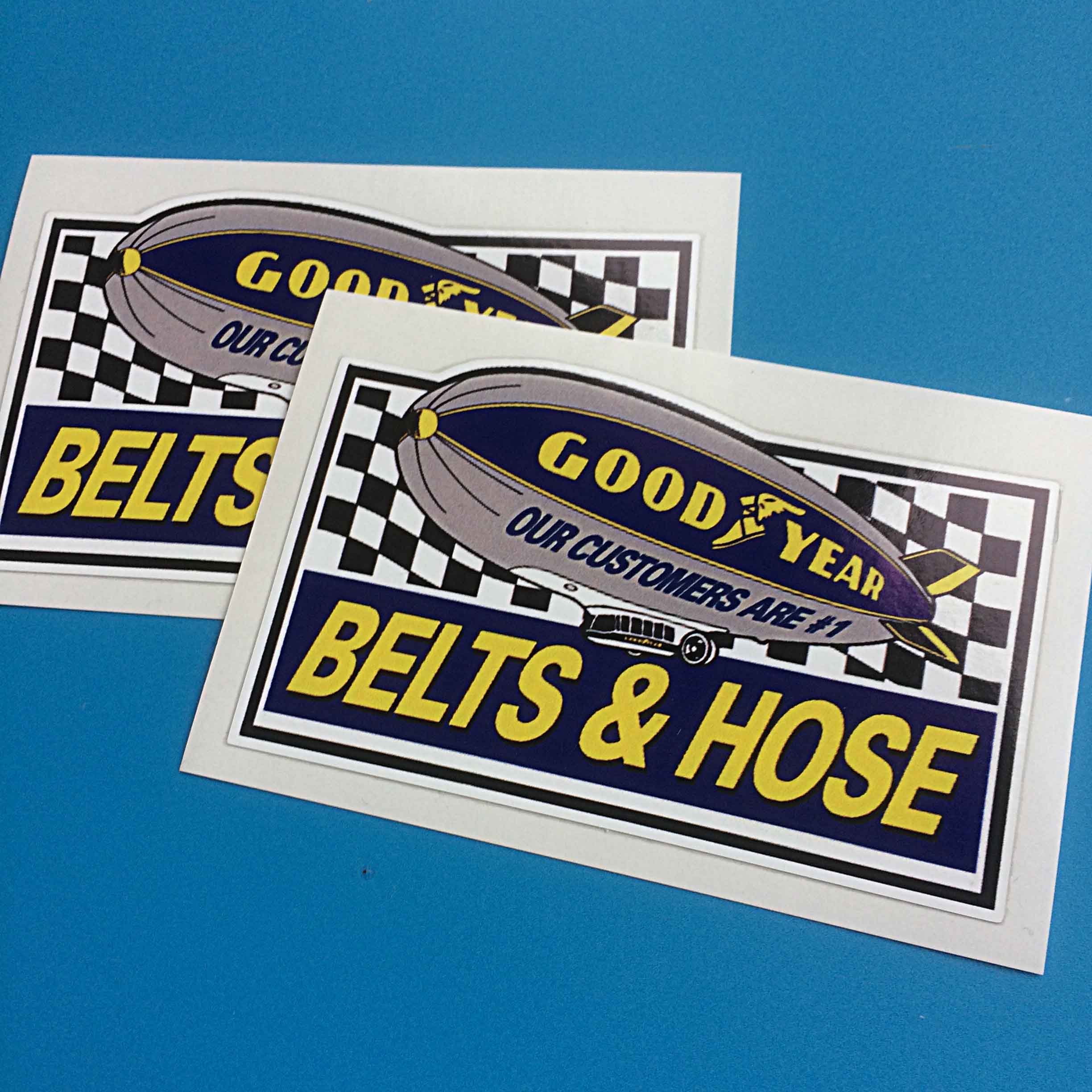 GOODYEAR BELTS AND HOSE STICKERS. An airship displaying the Goodyear logo Our Customers Are #1 on a black and white chequer background. Belts & Hose in yellow lettering on a blue banner is below.