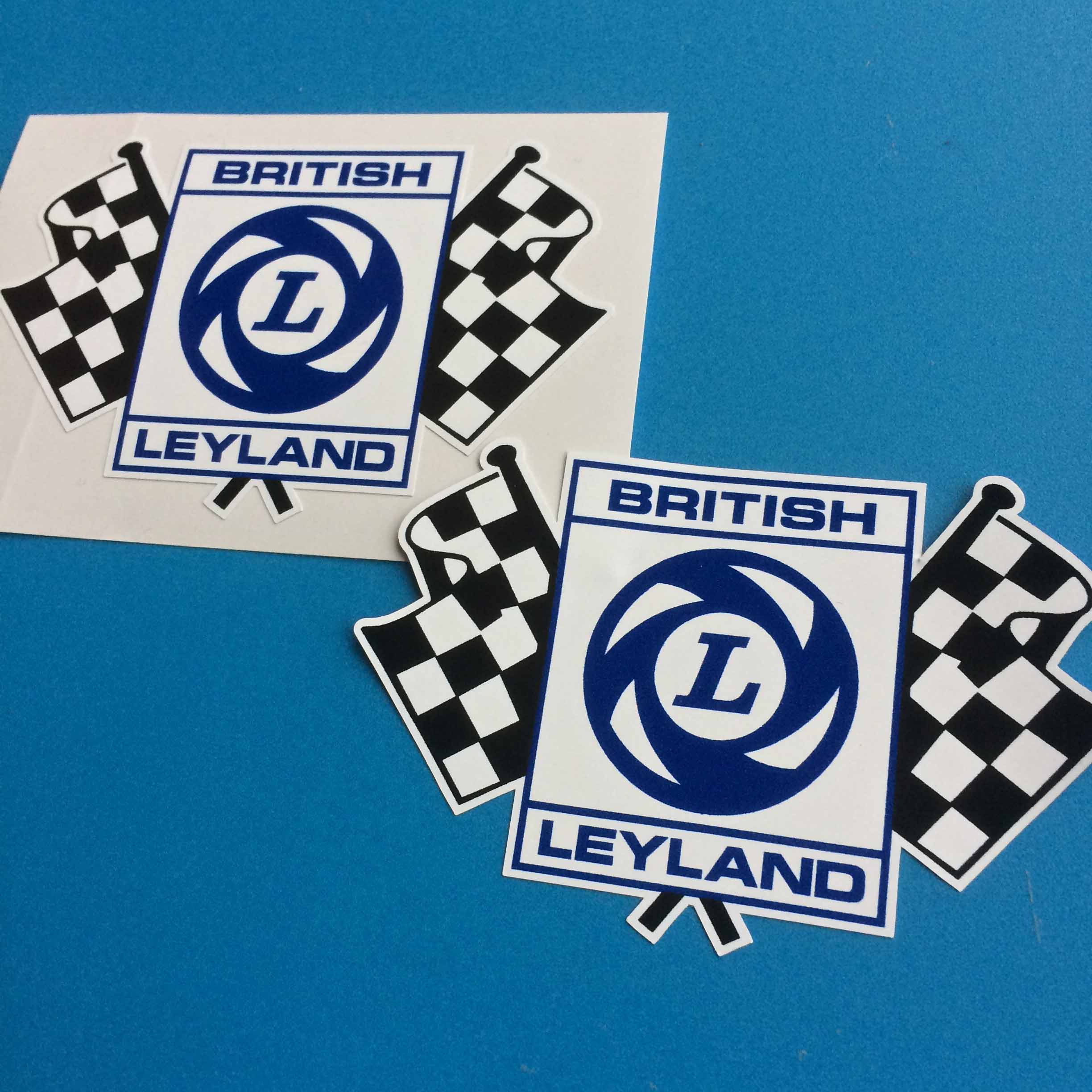 BRITISH LEYLAND CHEQUERED FLAG STICKERS. Two black and white chequered crossed flags In front of the flags is the blue and white L logo and the words British Leyland in blue.