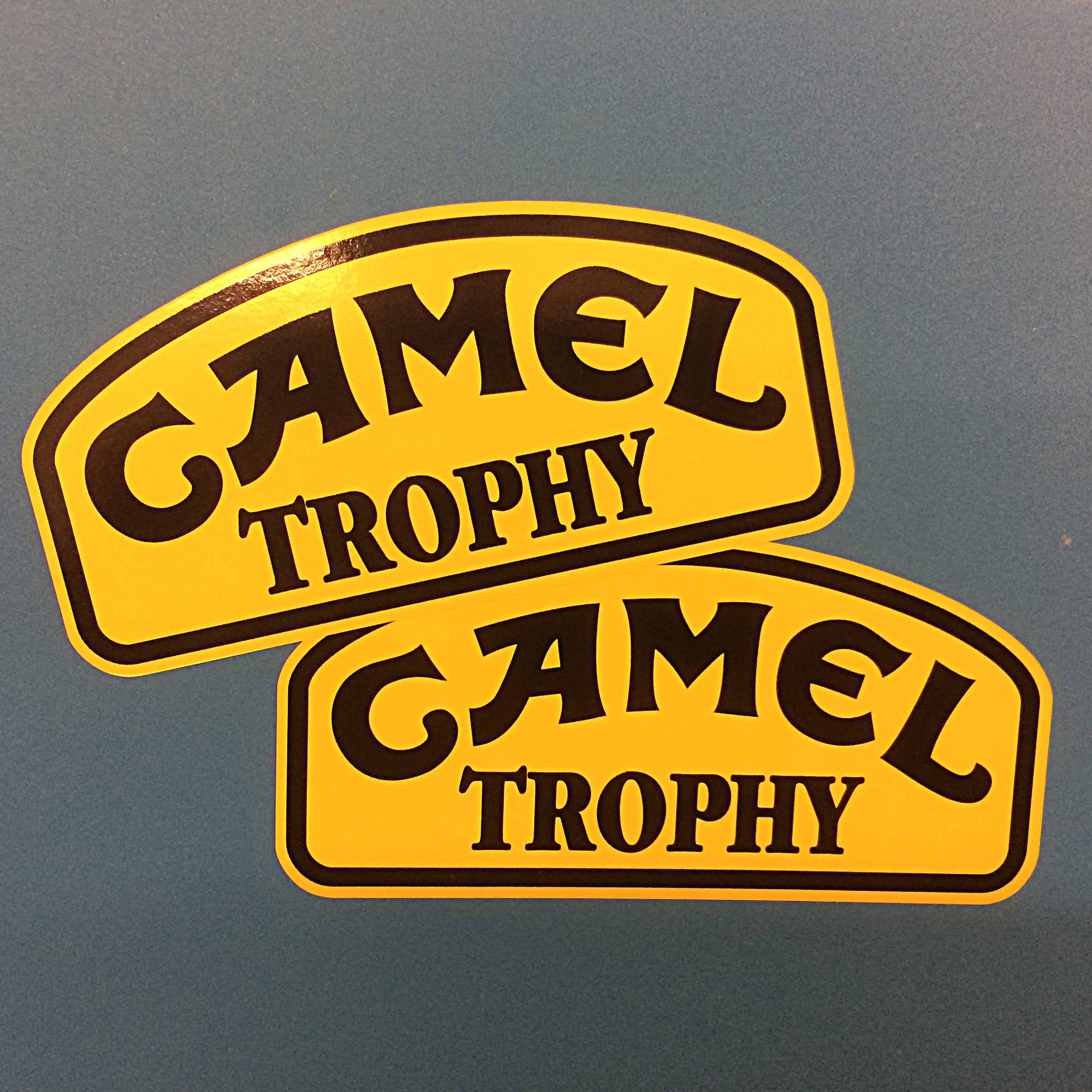CAMEL TROPHY STICKERS. Camel Trophy in black uppercase lettering on a yellow sticker with a black border. The top edge of the sticker is curved.