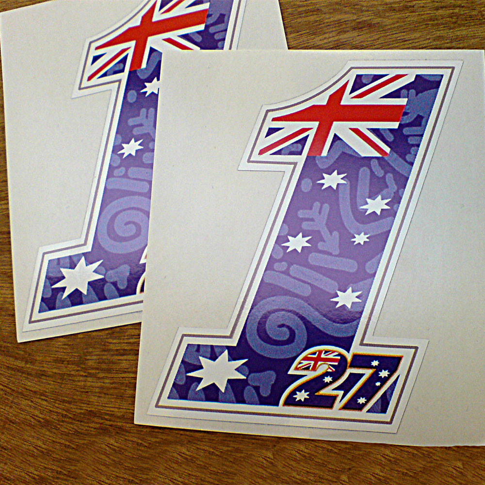 The Australian flag; a blue field with the Union Jack and five white stars in the shape of the numbers 1 and 27. The number 27 is outlined in gold and sits at the base of and within the number 1. The blue field is covered with abstract/Aboriginal art.