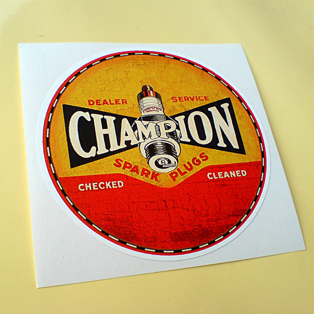 A circular sticker, half red, half yellow with a black and white border. Champion in white uppercase lettering on a black background with a spark plug in the centre. Additional text in red and white, Dealer Service Spark Plugs Checked Cleaned.