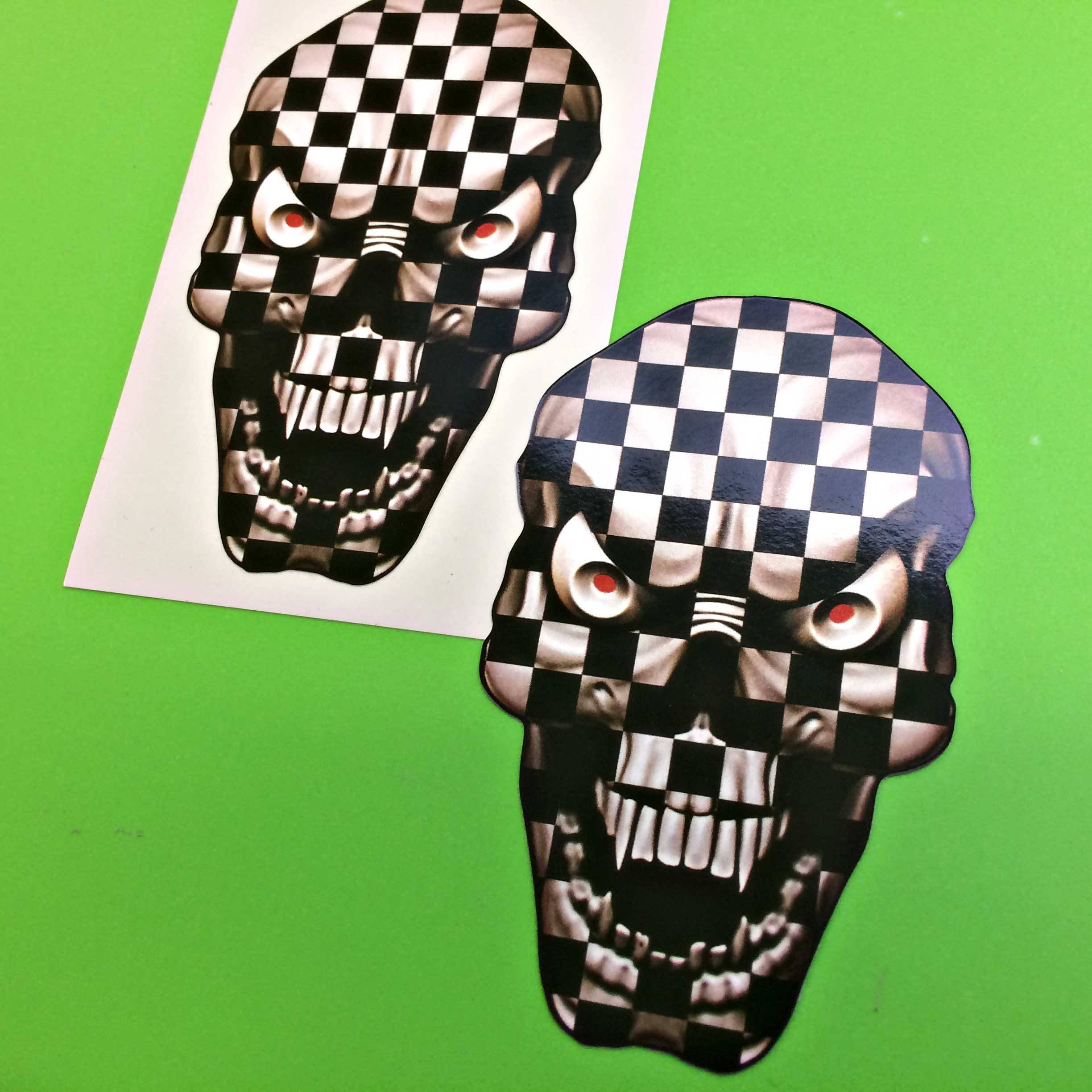 CHEQUERED SKULL STICKERS. A skull in black and white chequer with red eyes and sharp white teeth.