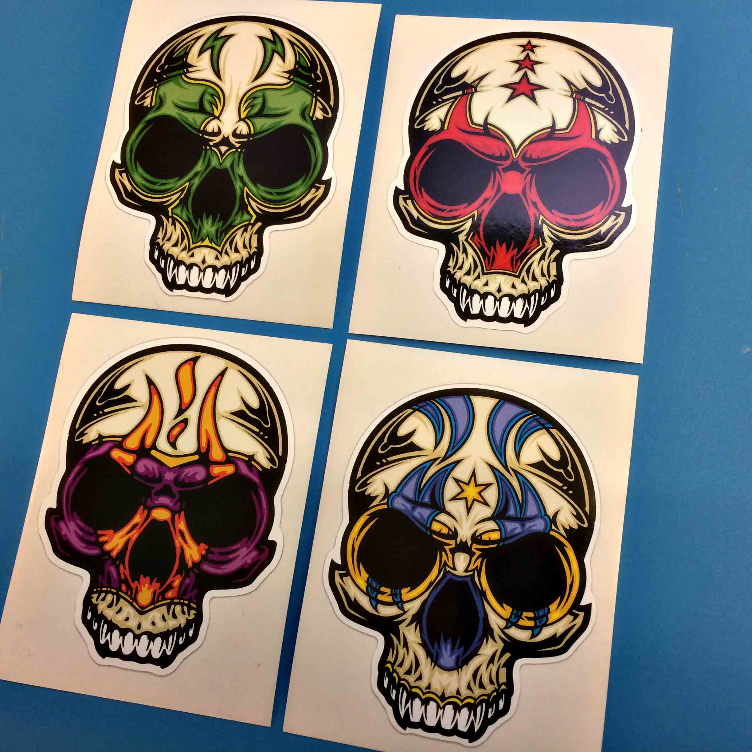 DAY OF THE DEAD STICKERS. A skull with white teeth. The eye socket area is either blue, green, purple or red.