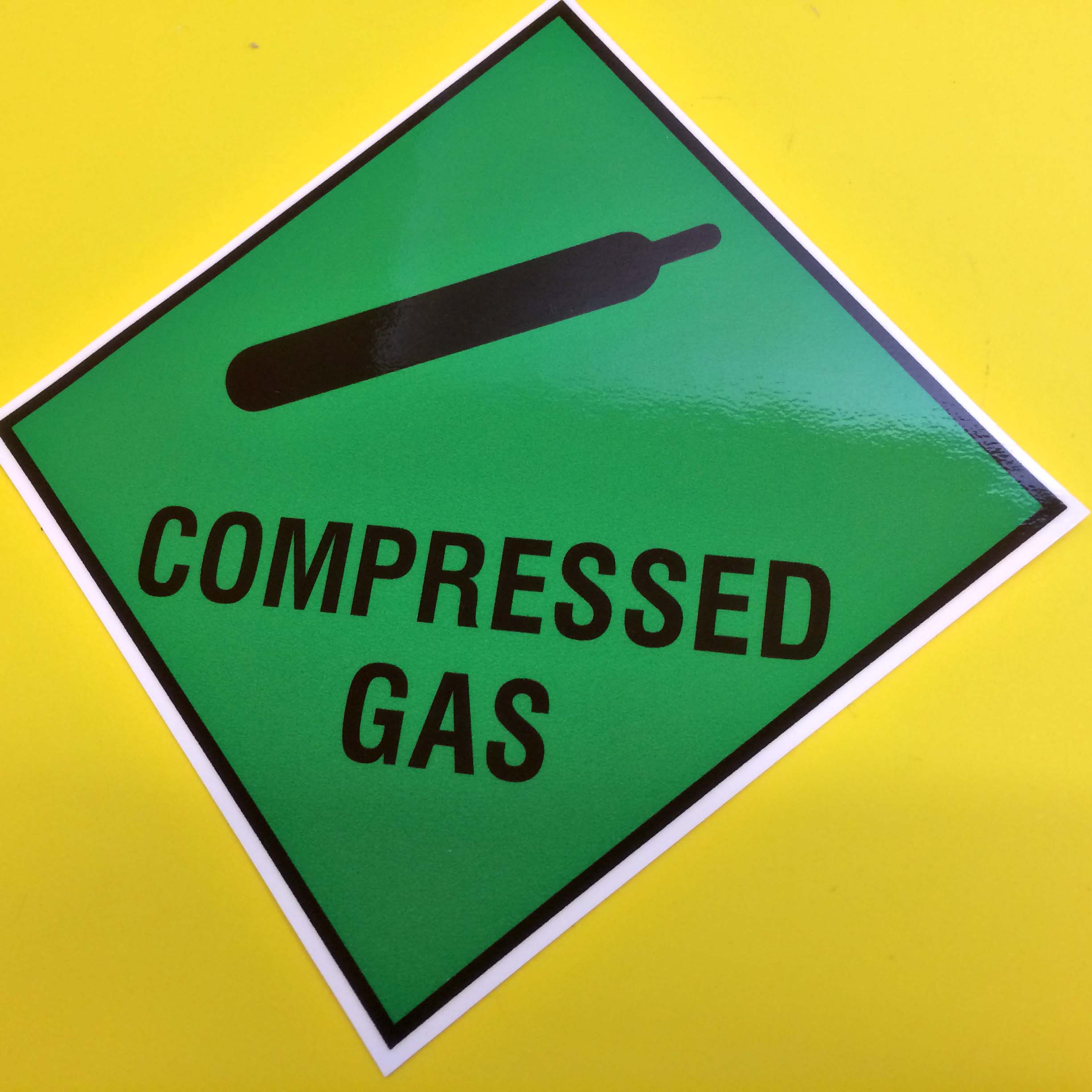 COMPRESSED GAS LAMINATED STICKER. Compressed Gas in black uppercase lettering and a gas cylinder on a green background.