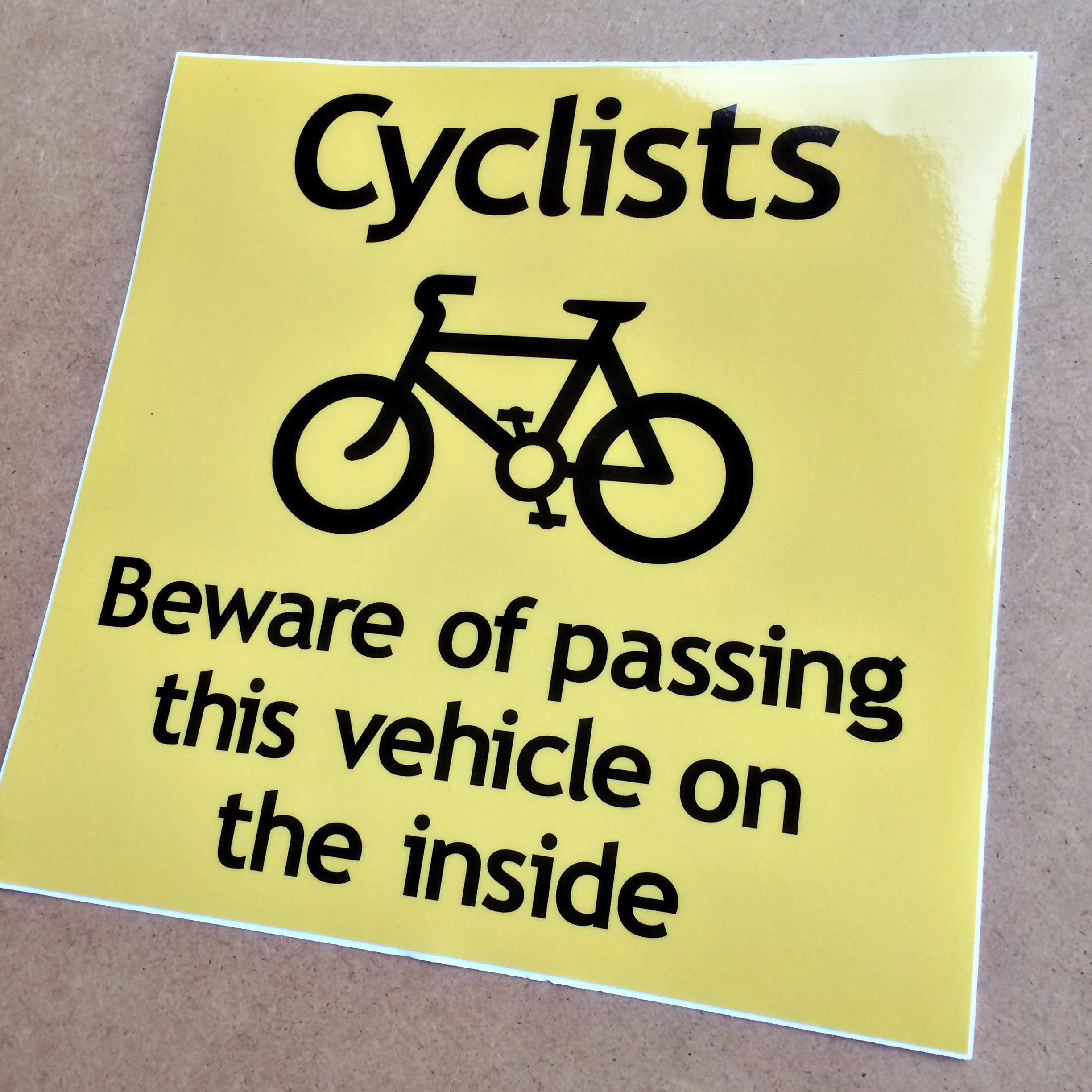 CYCLISTS BEWARE OF PASSING THIS VEHICLE LAMINATED STICKER. Cyclists Beware of passing this vehicle on the inside in black lowercase lettering and a bicycle on a yellow background.
