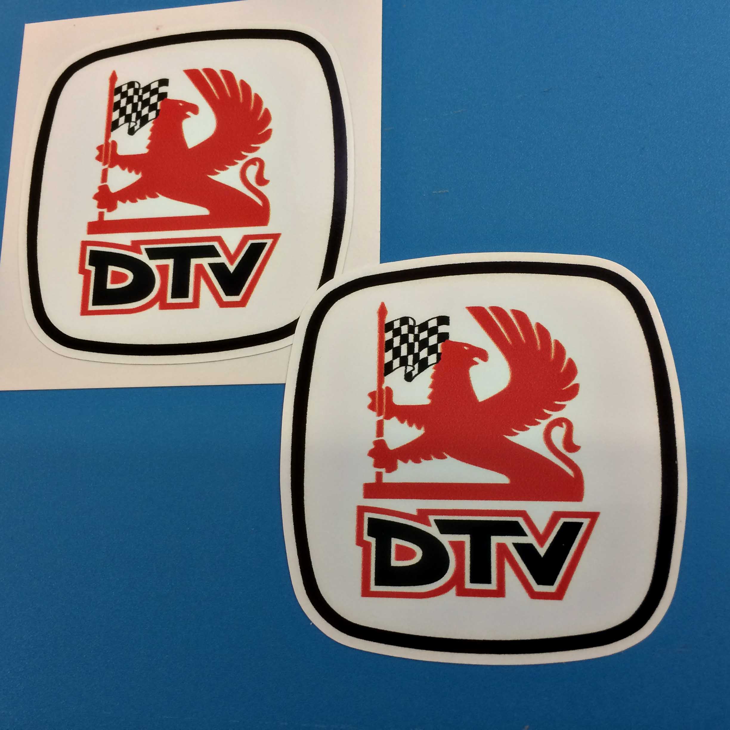 DTV DEALER TEAM STICKERS. Centre is a red Griffin holding a black and white chequered flag on a flagpole. Below the Griffin edged in red and white are letters DTV in black.