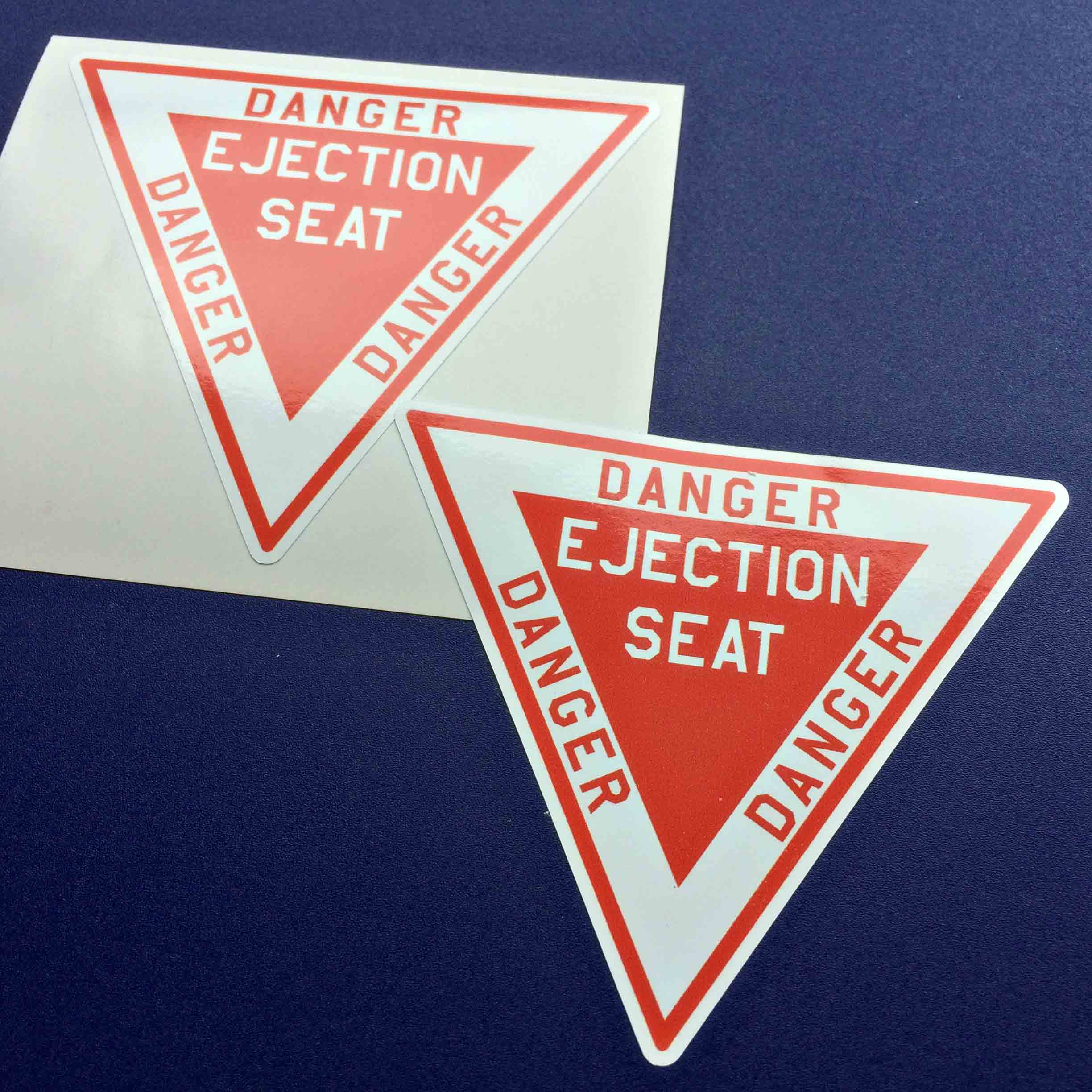 DANGER EJECTION SEAT STICKERS. Danger in red lettering on three sides of an inverted white triangle with a red border. Inside on a smaller red triangle is Ejection Seat in white lettering.