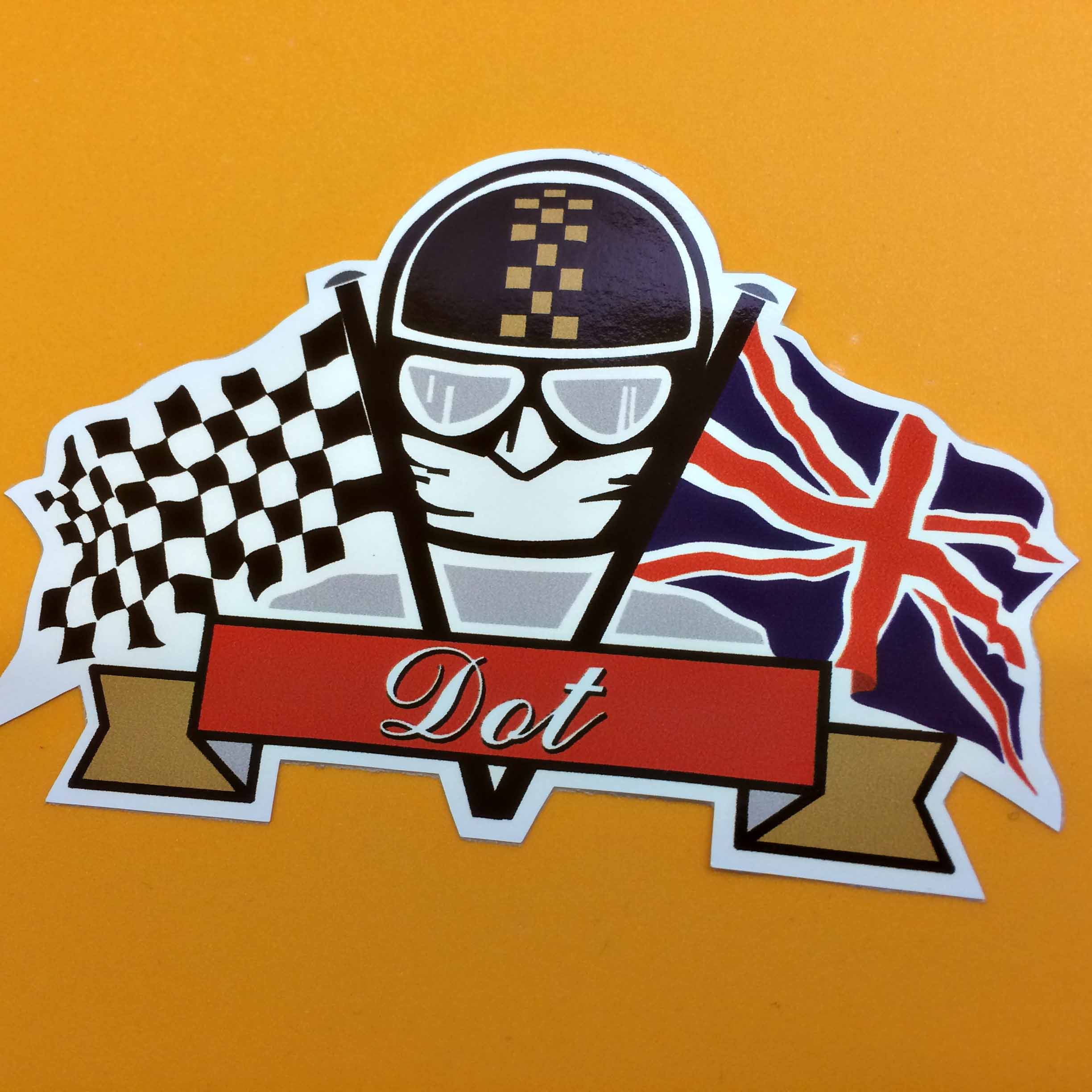 DOT DEVOID OF TROUBLE STICKER. Dot in white italic font on a red and gold banner. Above this is the face of a motorcyclist wearing goggles, a white scarf and a black helmet with a gold chequer strip. He sits between two crossed flags - a black and white chequer and a Union Jack.