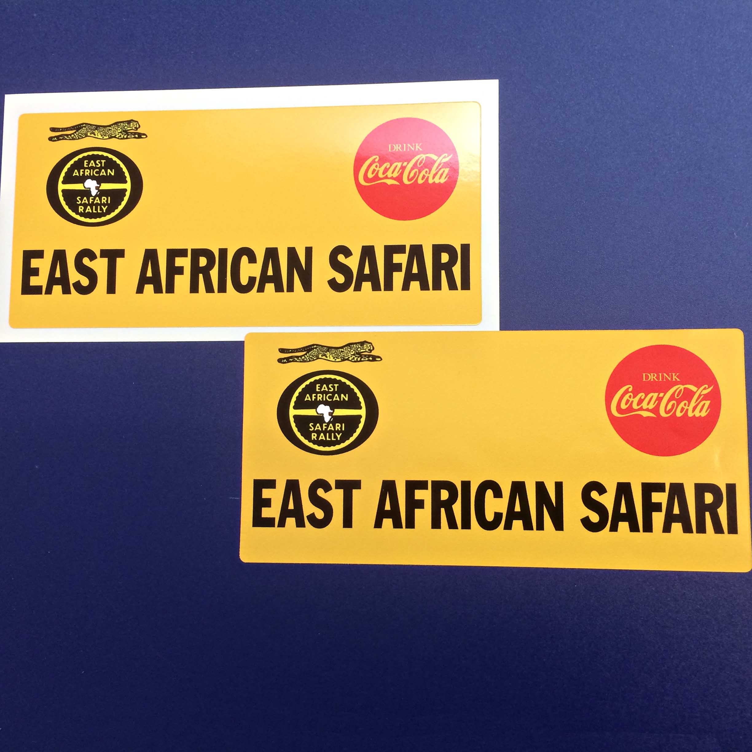 East African Safari in black lettering on a yellow sticker. Above are two logos. Drink Coca Cola in a red circle and East African Safari Rally, a leaping leopard and a yellow steering wheel with a map of Africa in the centre on a black oval.