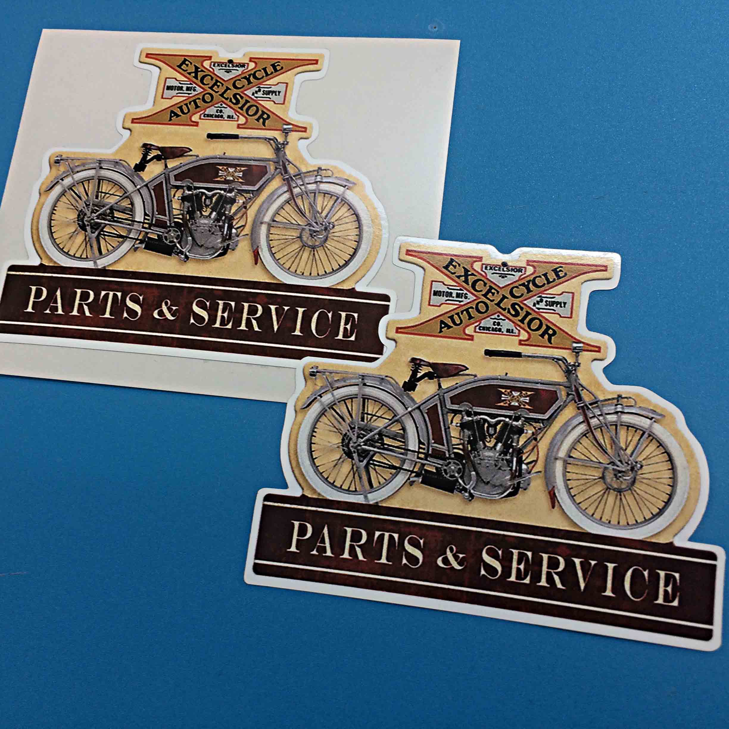 EXCELSIOR AUTO CYCLE PARTS AND SERVICE STICKERS. Excelsior Auto Cycle in black lettering on a gold X with additional lettering in the background - Excelsior Motor Mfg. Supply Co. Chicago, Il. Below is an Excelsior auto cycle and a banner Parts & Service.