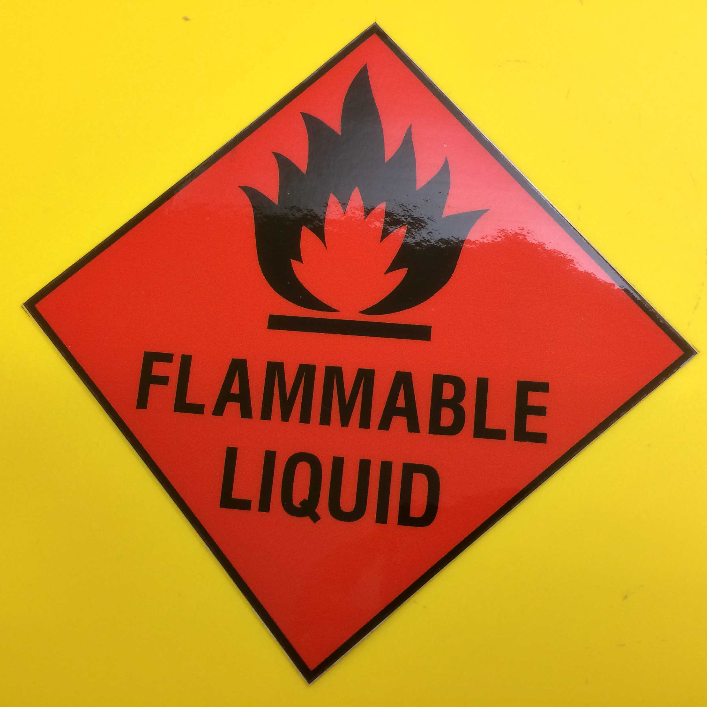 Black flames at the top. Below is Flammable Liquid in black capitals. Red, diamond shaped sticker edged in black.