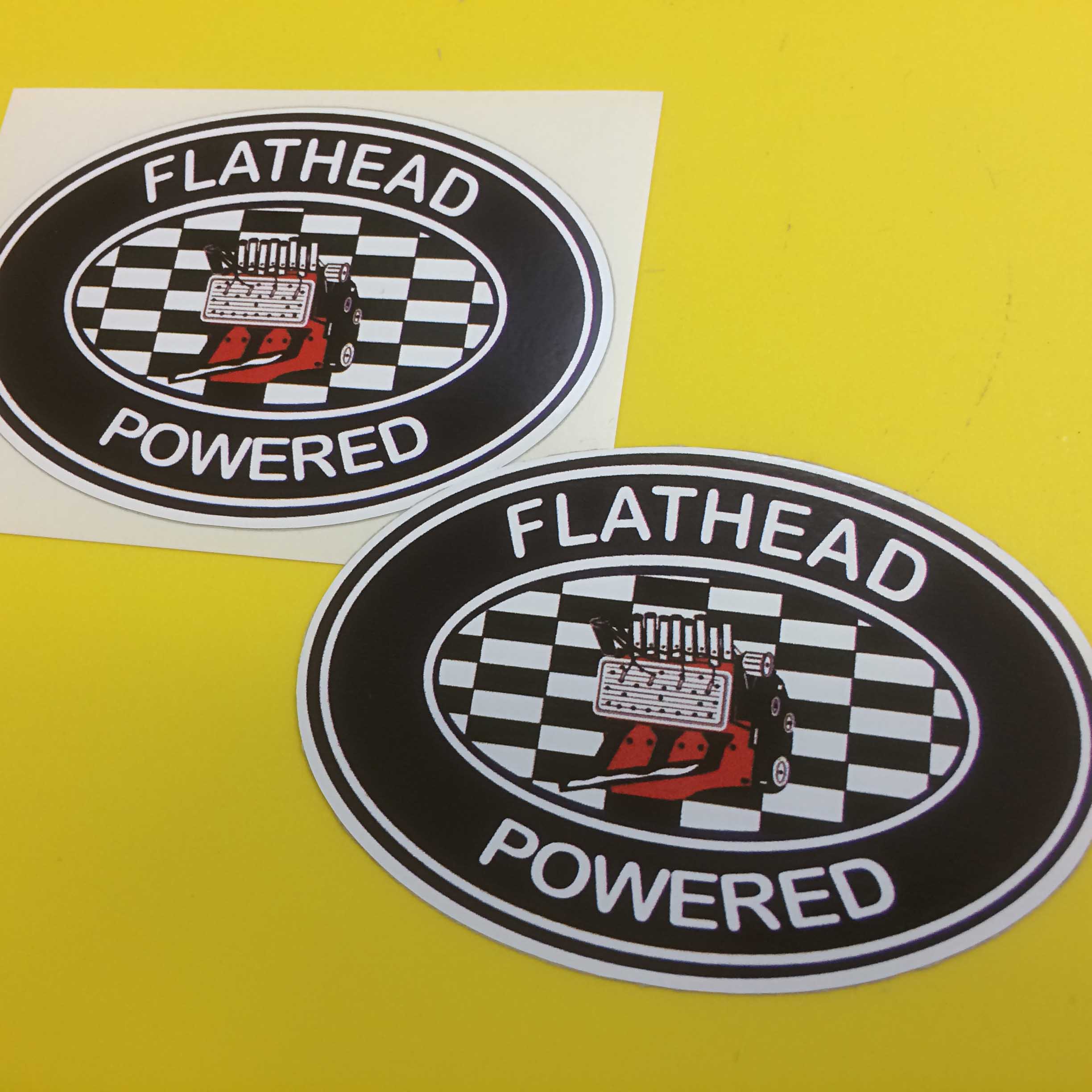 FLATHEAD POWERED RACE RALLY STICKERS. Flathead Powered in white lettering surrounds a black oval sticker. In the centre is a red flathead engine on a black and white chequer oval.