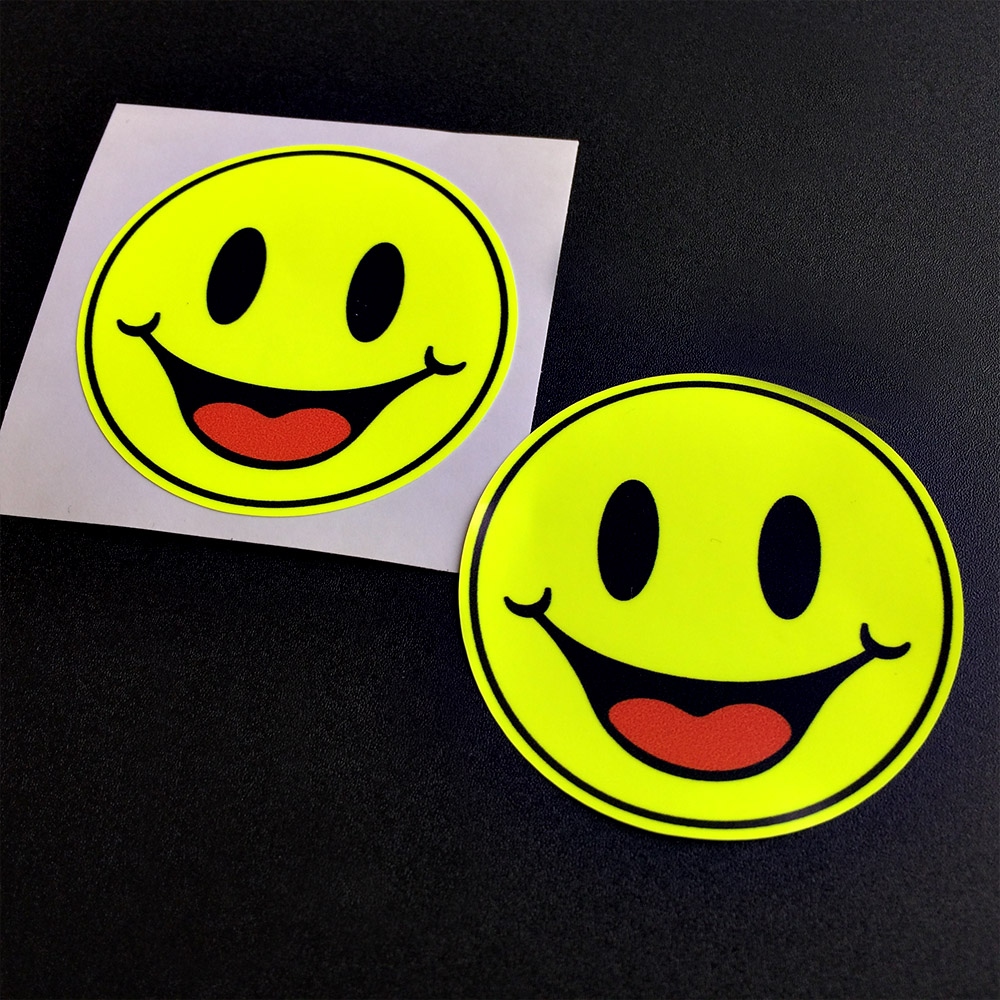 REFLECTIVE HAPPY SMILEY STICKERS A fluorescent yellow round smiling face. The eyes are black and the mouth is open displaying a red tongue.