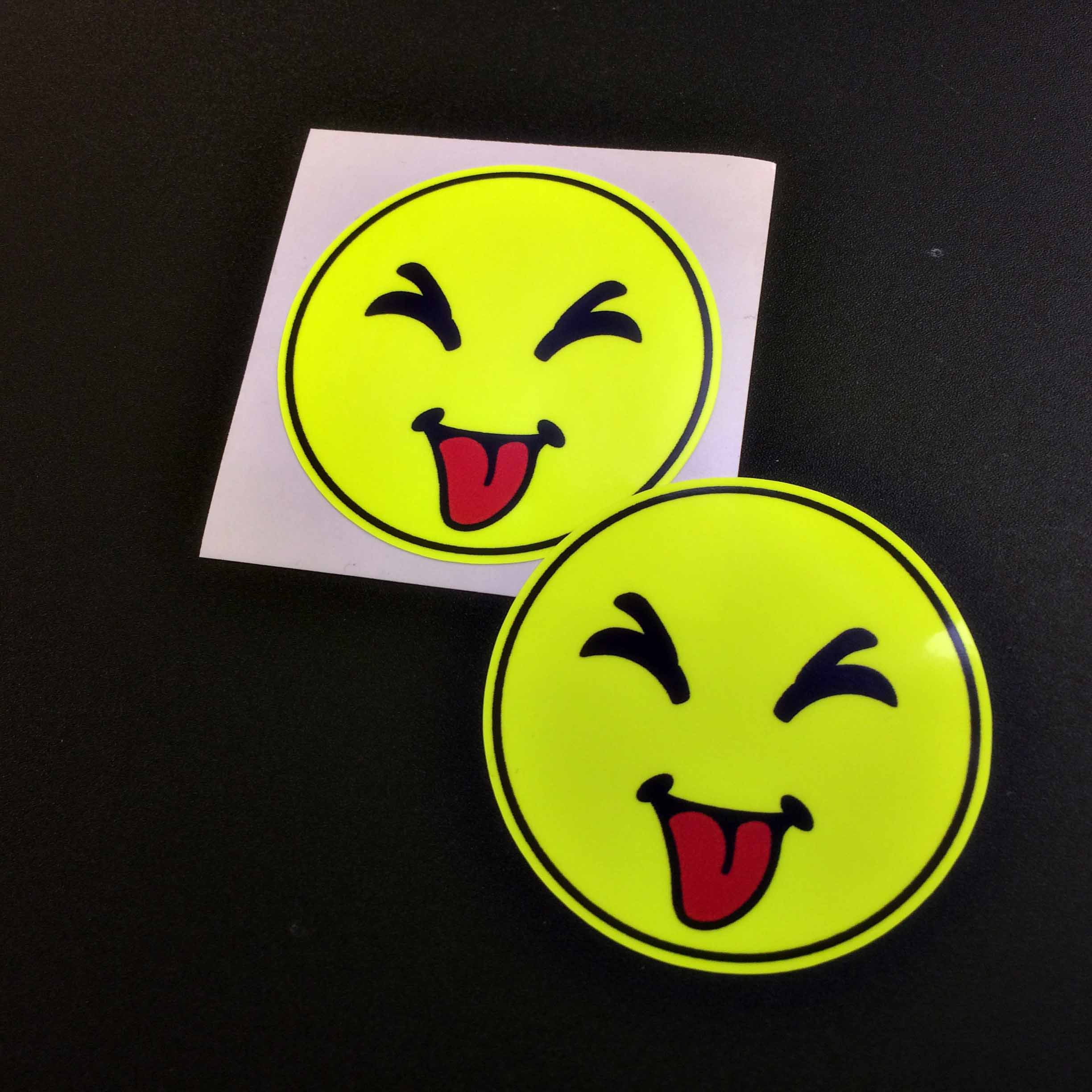 A fluorescent yellow round smiling face. The eyes are closed and the red tongue is hanging out.