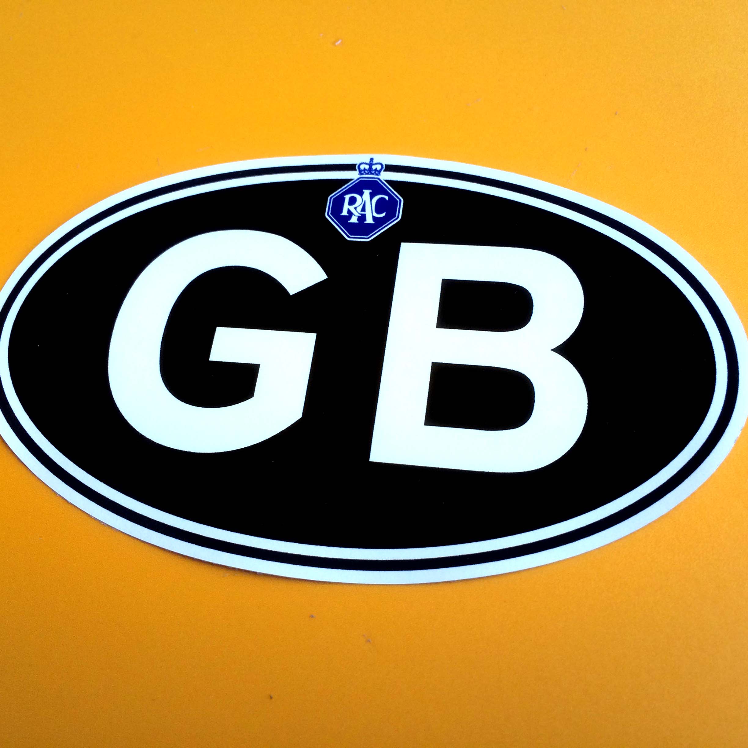 GB in bold white lettering on a black oval sticker with a white border. Above GB is the RAC logo - white lettering on a blue octagon topped with a crown.