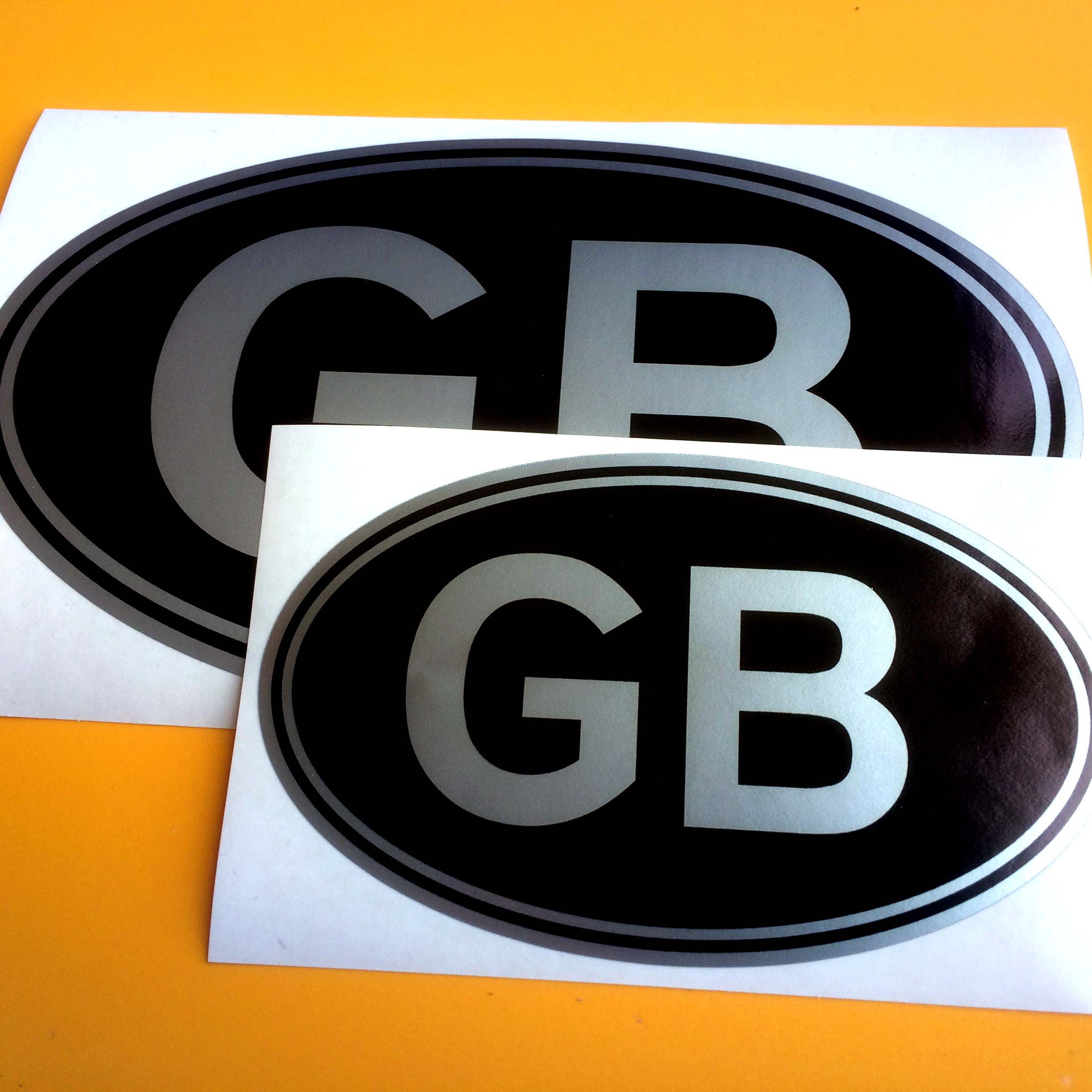 GB in bold silver lettering on a black oval sticker with a silver border.