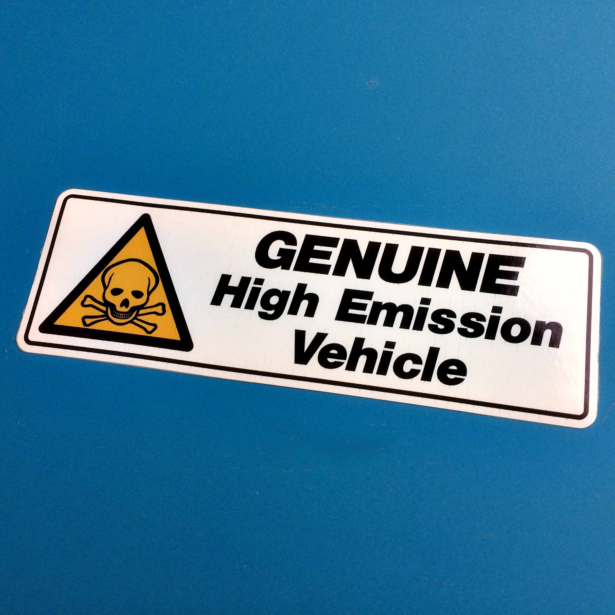 Genuine High Emission Vehicle in black lettering on a white background bordered in black next to a skull and crossbones hazard triangle in yellow and black.