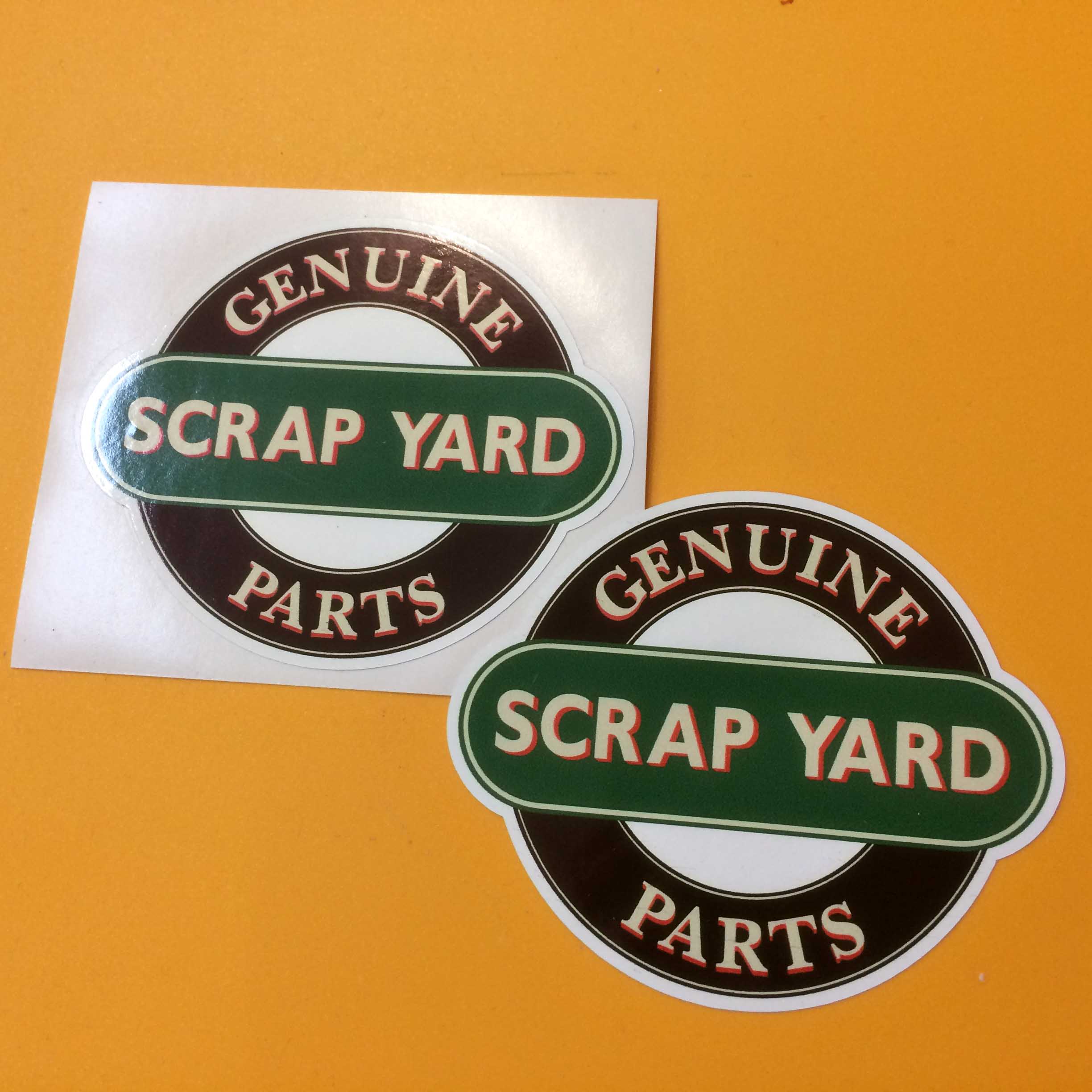 Two concentric circles in black and white. Genuine Parts in red and white lettering surrounds the black outer circle. Scrap Yard on a green banner sits across the centre.