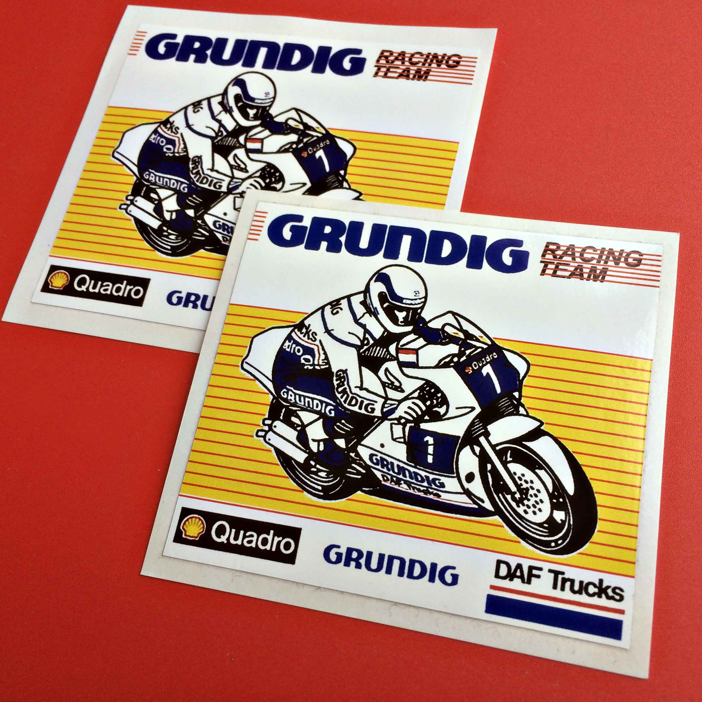 A motorcyclist riding a motorbike with the number 1 on the front. They are both in blue and white and emblazoned with advertising. On a yellow background Grundig Racing Team, Quadro and DAF Trucks logos surround them.