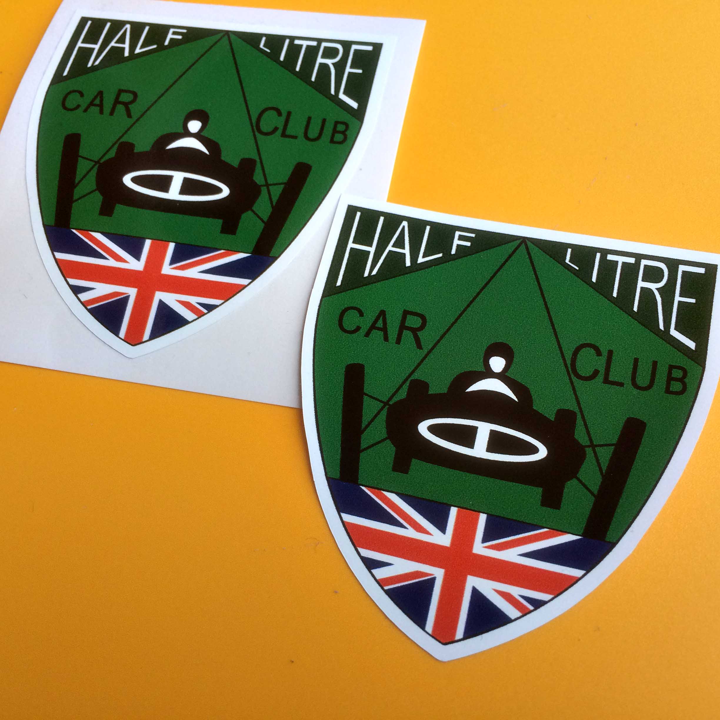 HALF LITRE CAR CLUB STICKERS. Half Litre Car Club in black and white lettering on a shield shaped sticker. In the centre is a black racing car driven by a man in white on a green racetrack. Below this is a Union Jack.