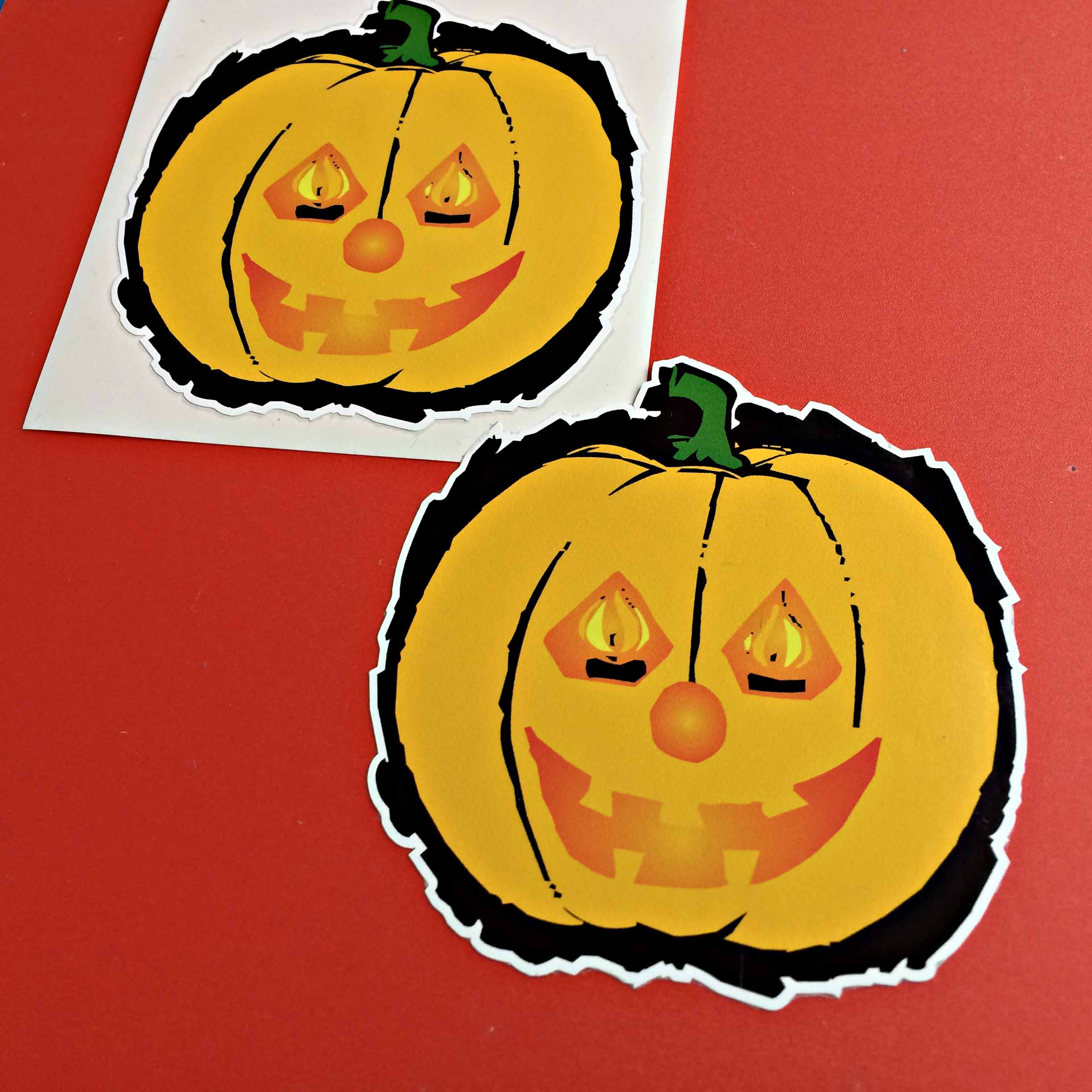 HALLOWEEN PUMPKIN STICKERS. An orange pumpkin with a green stalk on a black background. It has a mouth, nose and eyes displaying flames.