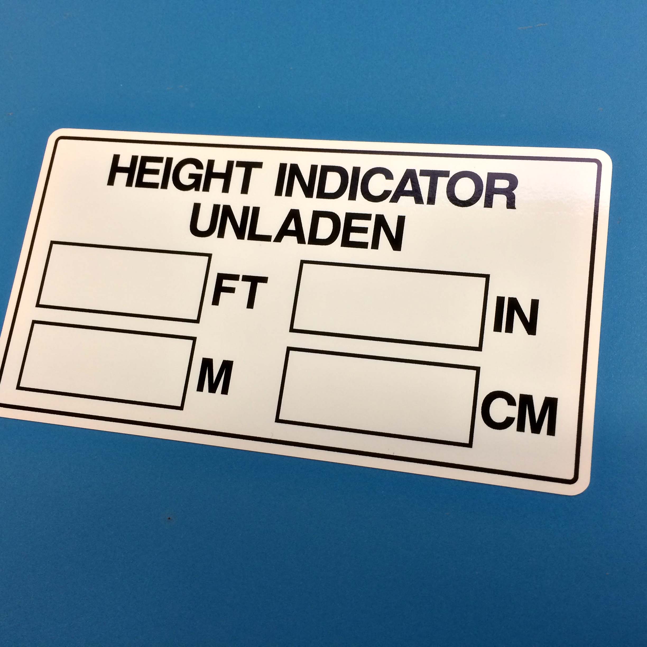 Height Indicator Unladen in black uppercase lettering on a white sticker. Below are four rectangular boxes labelled Ft, In, M and Cm.