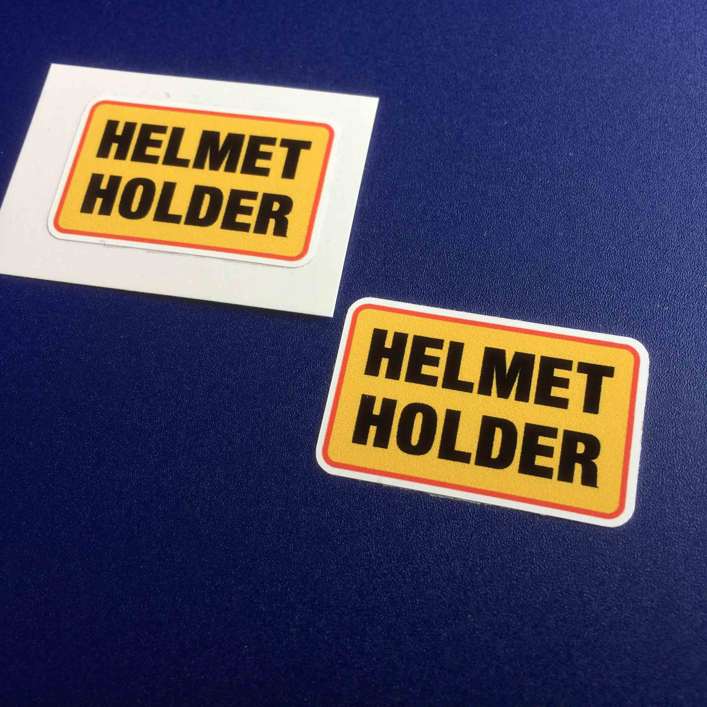 HELMET HOLDER STICKERS. Helmet Holder in bold black uppercase lettering on a yellow background with an orange border.