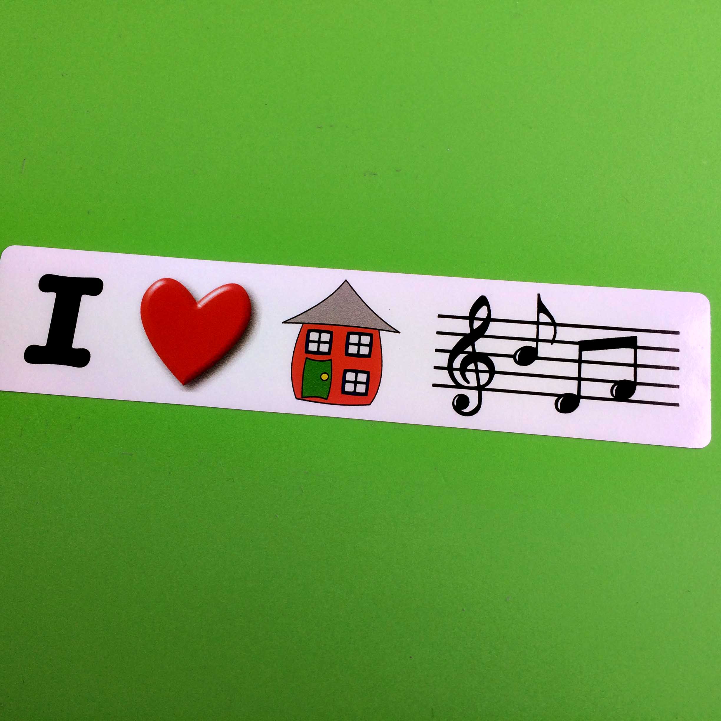 The letter I in black, a red love heart, a red house with a green door and three windows and musical notes sit in a row on a white background.