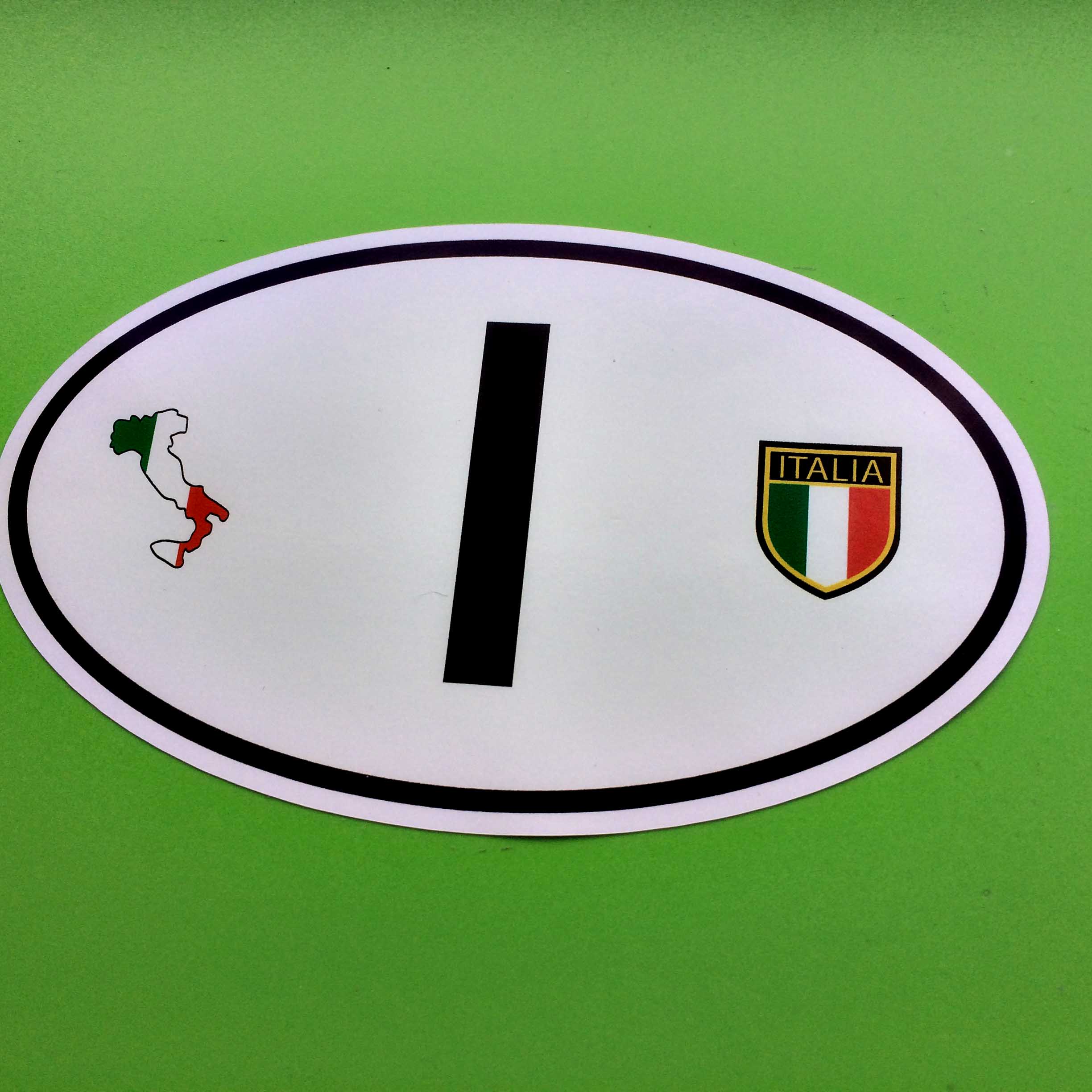 A white oval sticker with a black border. The letter I in black sits between a map of Italy in national colours and a shield - a vertical tricolour of green, white and red with Italia in gold lettering on a black background.