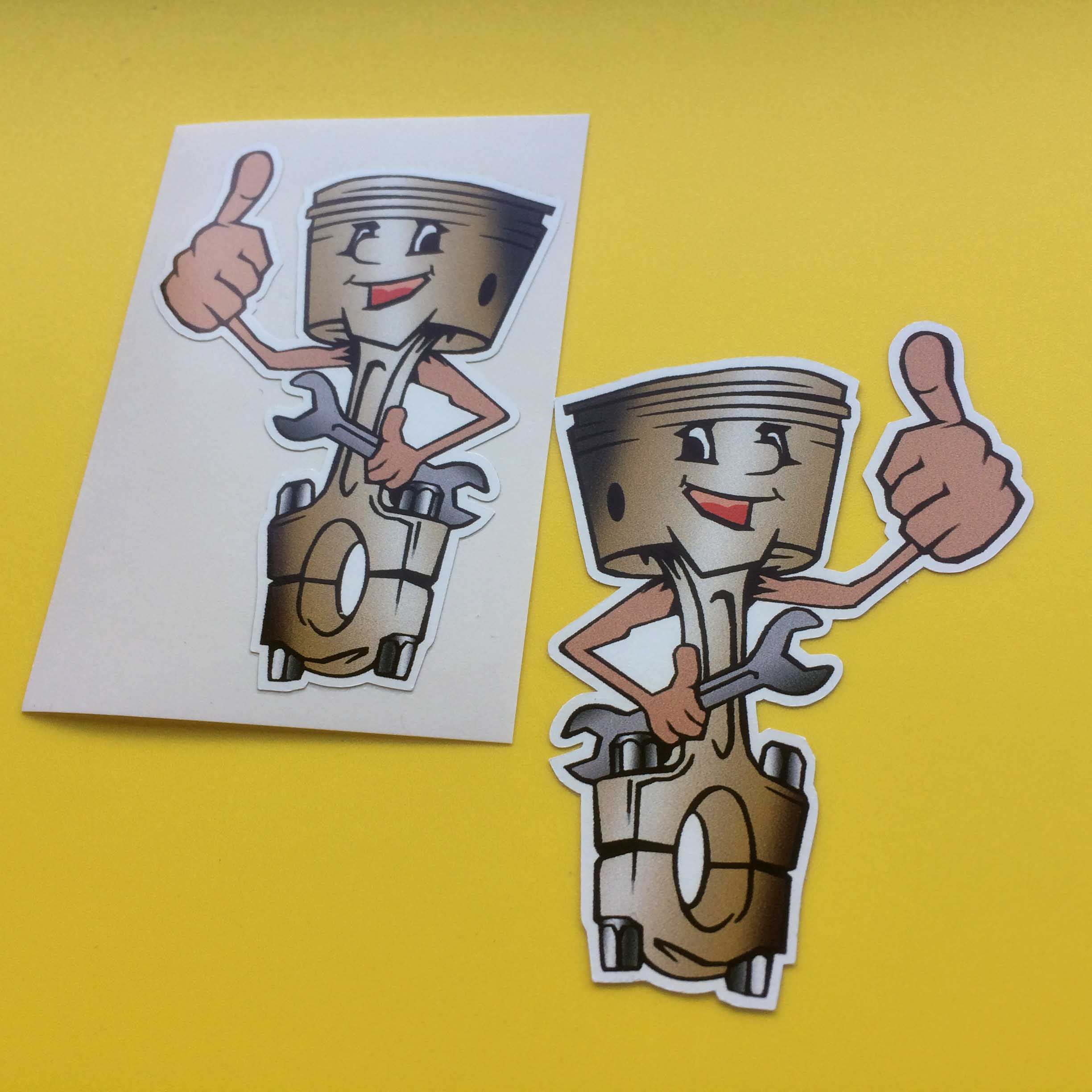 JOLLY HAPPY PISTONS STICKERS. A cartoon image of a piston with a smiling face holding a spanner in one hand and giving the thumbs up with the other.