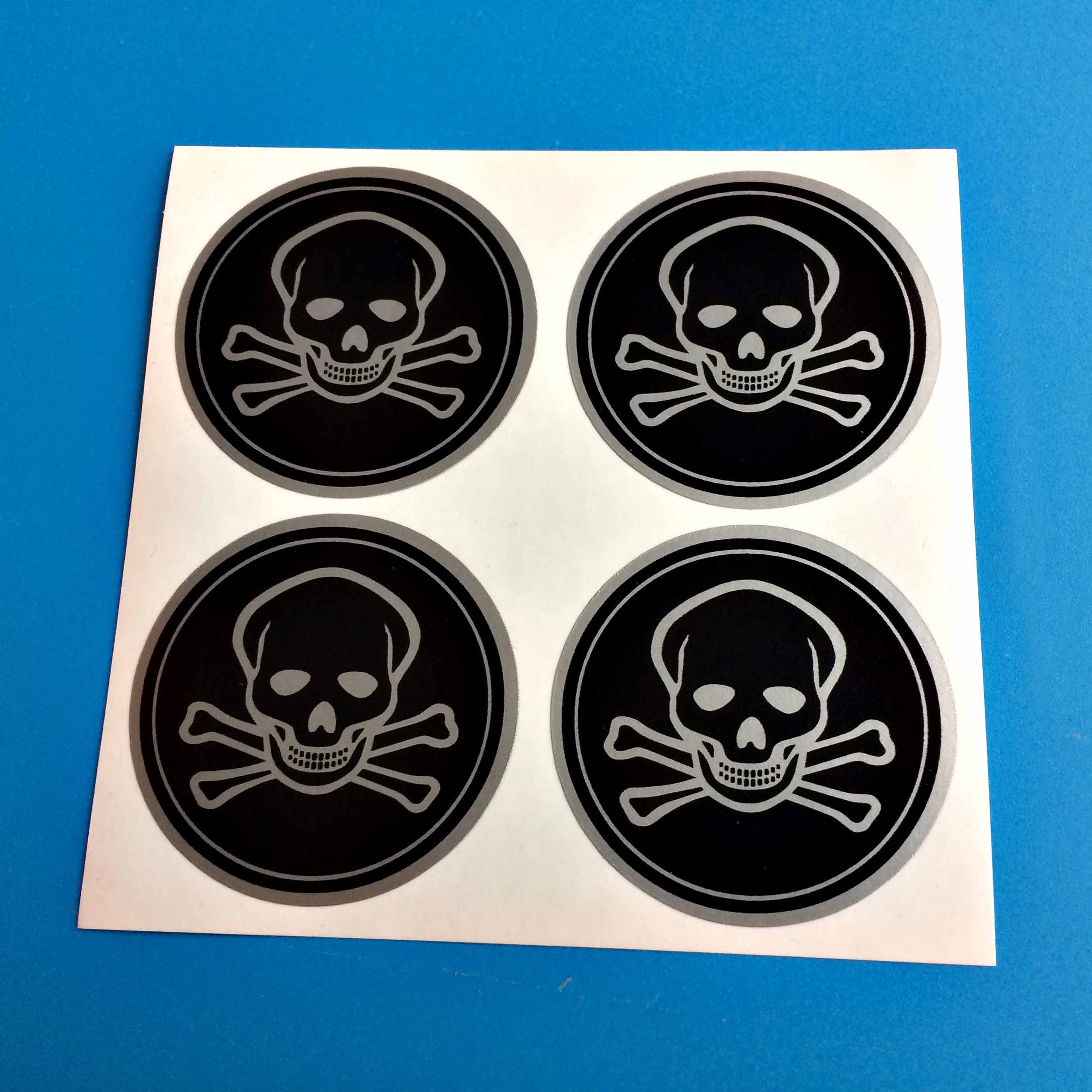JOLLY ROGER PIRATES SKULL AND CROSSBONES STICKERS. The contour of a skull and crossbones in silver on a black background. A circular sticker with a silver border.