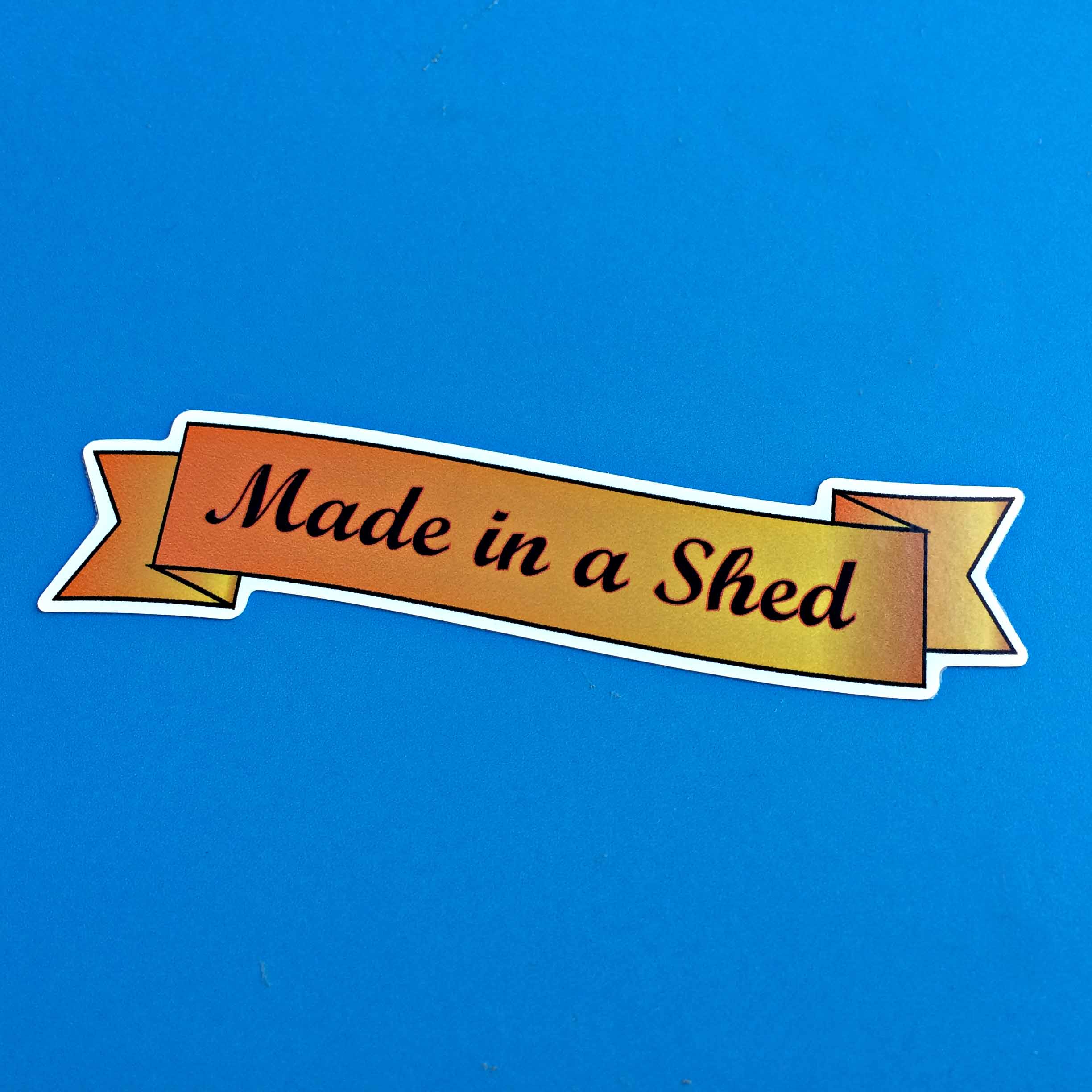 MADE IN A SHED STICKER. Made in a Shed handwritten font in black on a gold length of ribbon.