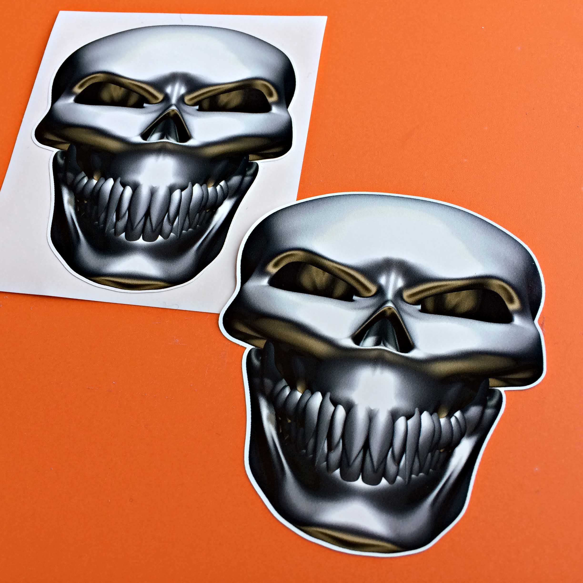 METAL SKULL STICKERS. Front view of a metal skull with teeth. The eye sockets and cheekbones are gold.