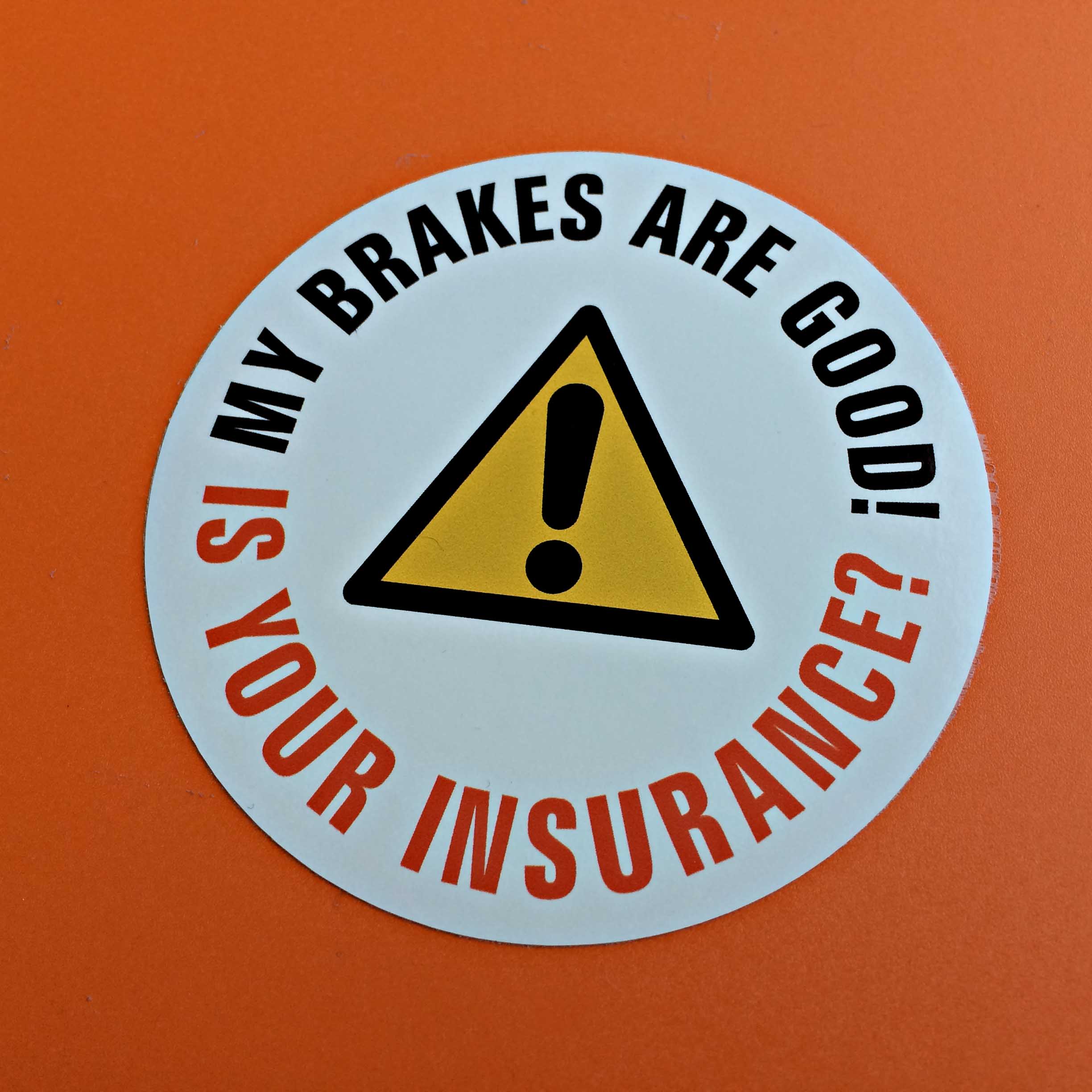 MY BRAKES ARE GOOD STICKER. My Brakes Are Good! in black lettering Is Your Insurance? in red lettering. Centre of the circle is a yellow hazard warning triangle.