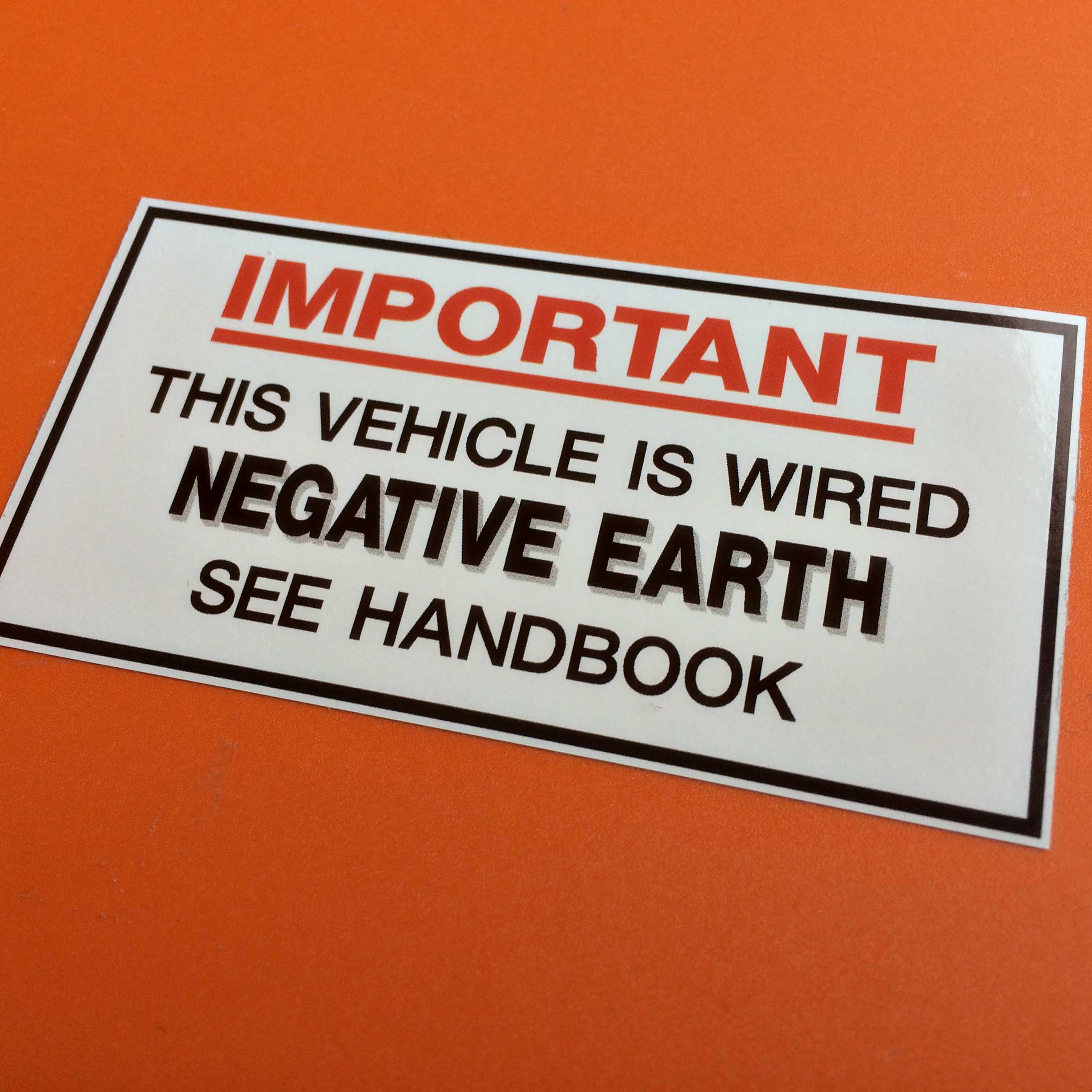 NEGATIVE EARTH STICKER. This Vehicle Is Wired Negative Earth See Handbook in black lettering on a white background. Important in red lettering and underlined.