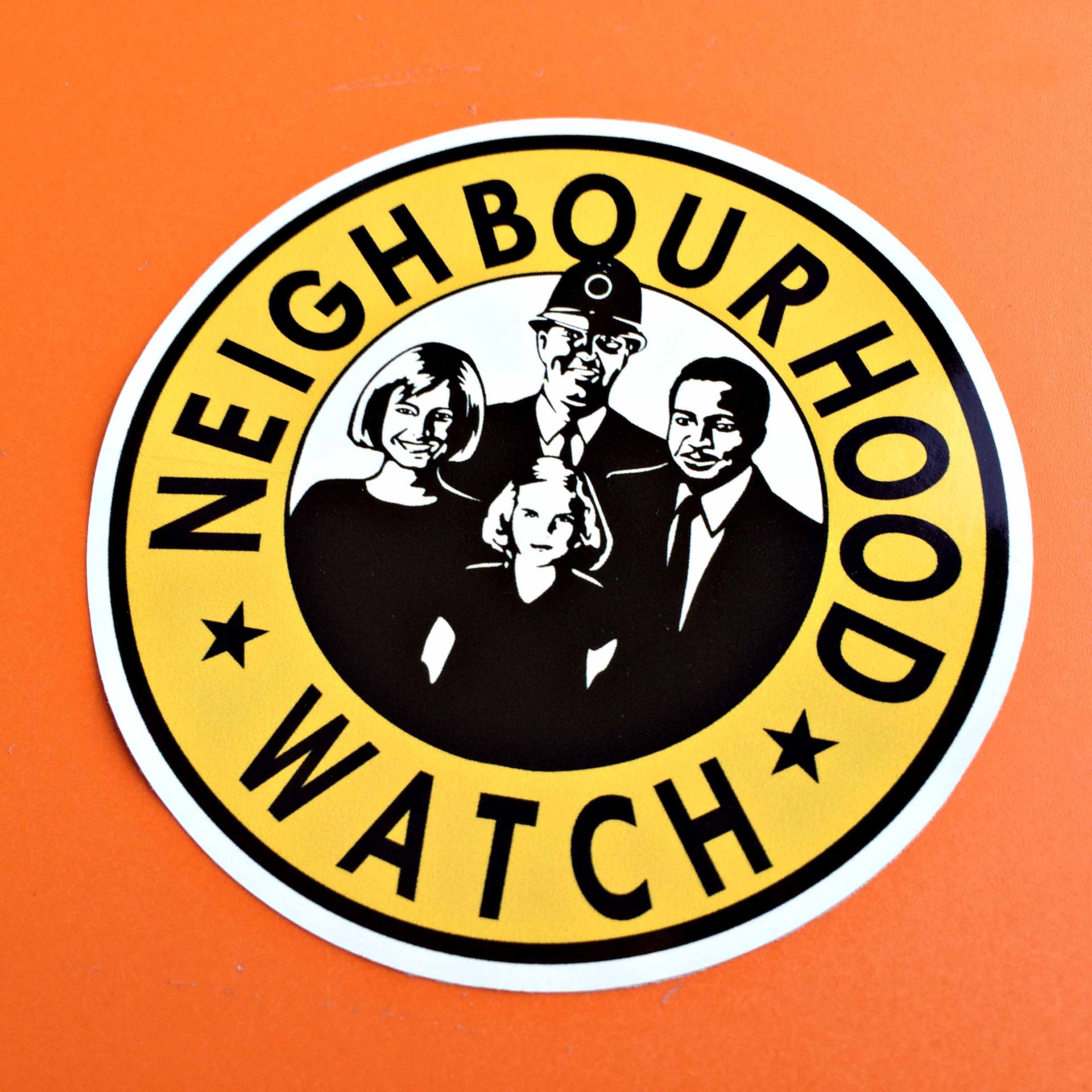 Neighbourhood Watch in black lettering around a yellow circle. Inner circle contains black and white figures of a man, woman, child and a policeman.