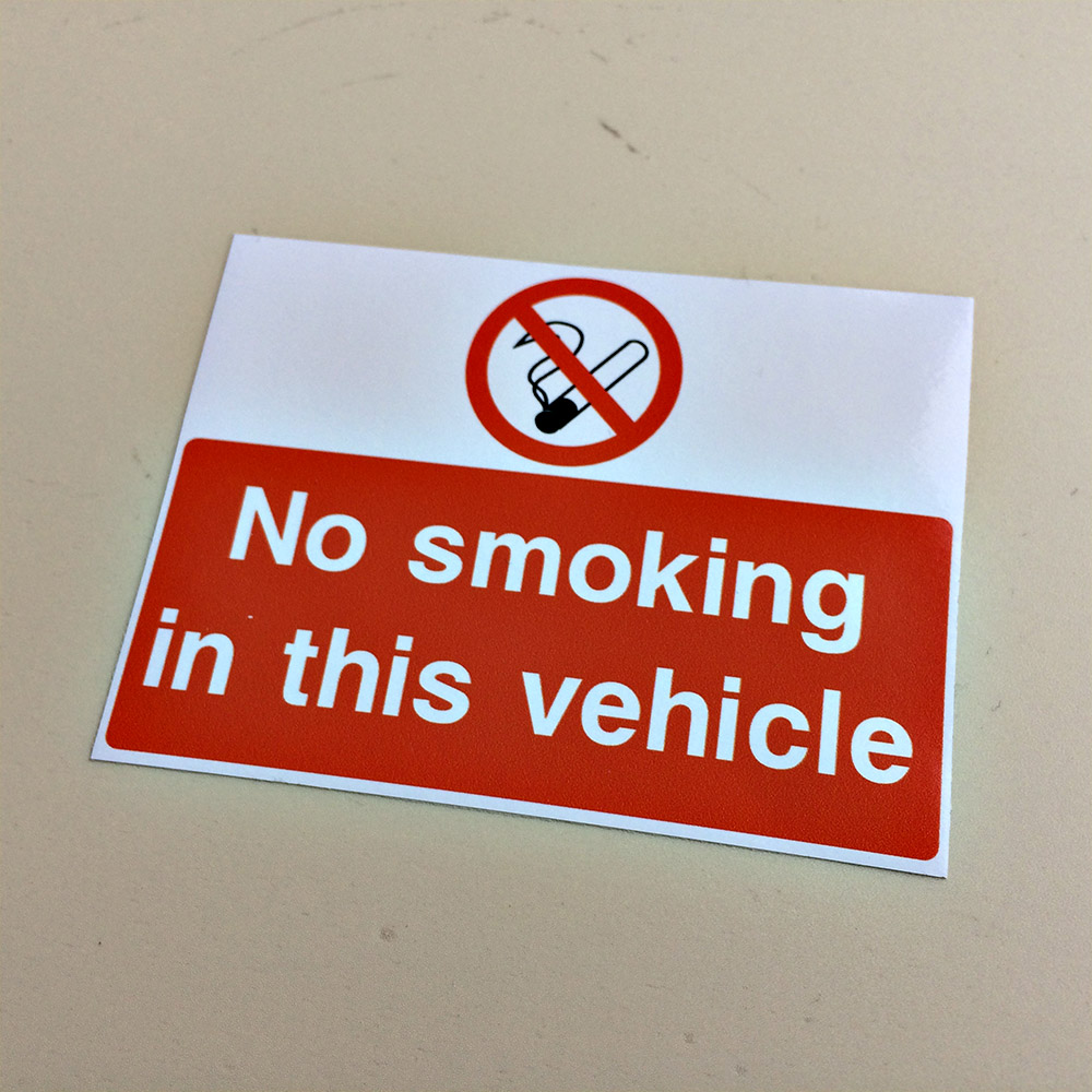 No smoking in this vehicle in white on a red background. Above is a no smoking symbol on a white background.