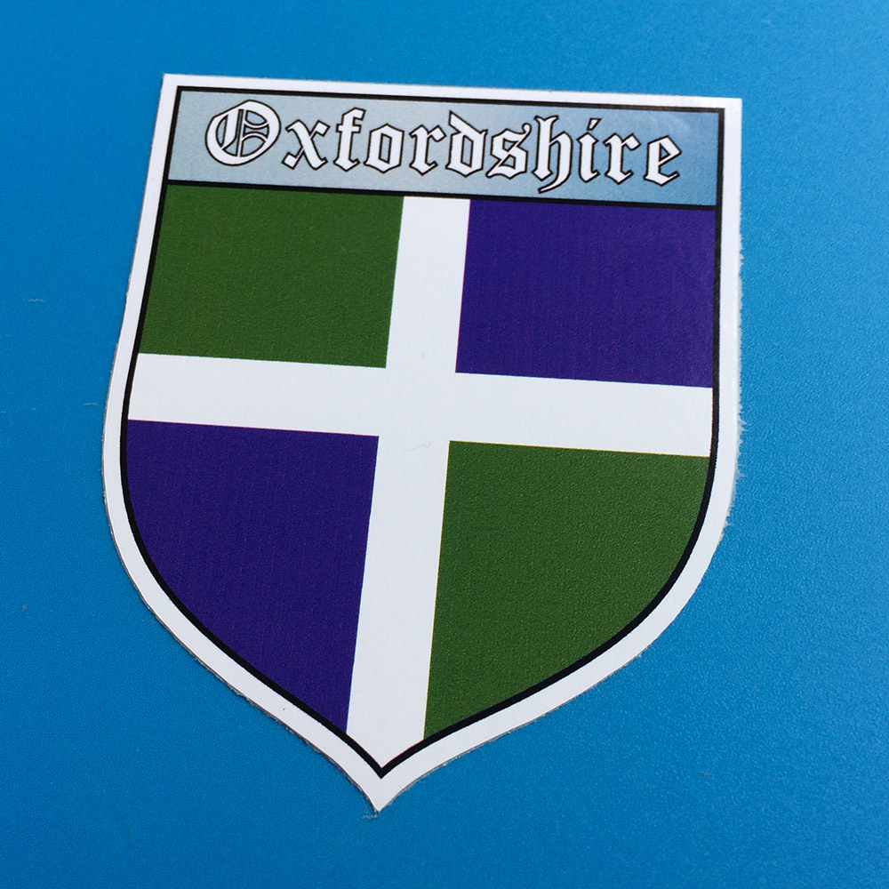OXFORDSHIRE COUNTY SHIELD STICKER. A white cross on a quartered green and blue field. Oxfordshire in white lettering at the top of the shield.