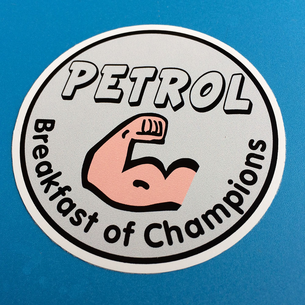 PETROL BREAKFAST OF CHAMPIONS STICKER. A bent arm with clenched fist and bulging bicep. Petrol Breakfast of Champions in black lettering surrounds the image on a grey background.