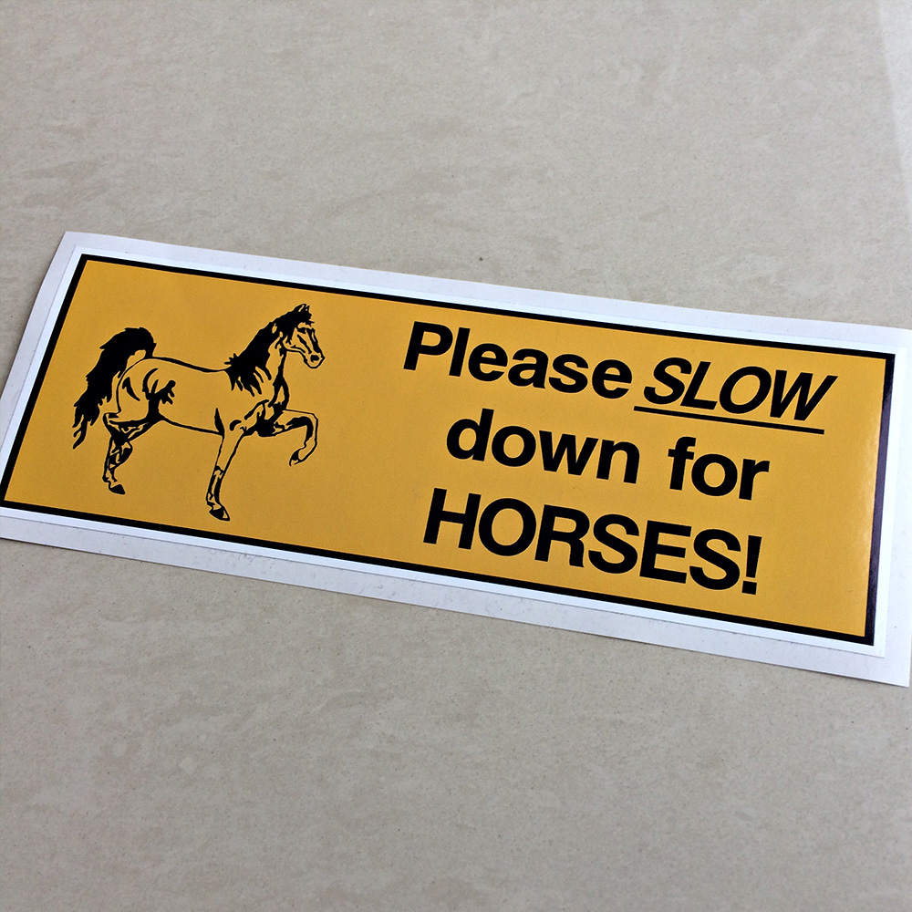 PLEASE SLOW DOWN FOR HORSES STICKER. Please Slow down for Horses! in black lettering next to a horse with a front and a rear hoof in the air. On a yellow background.