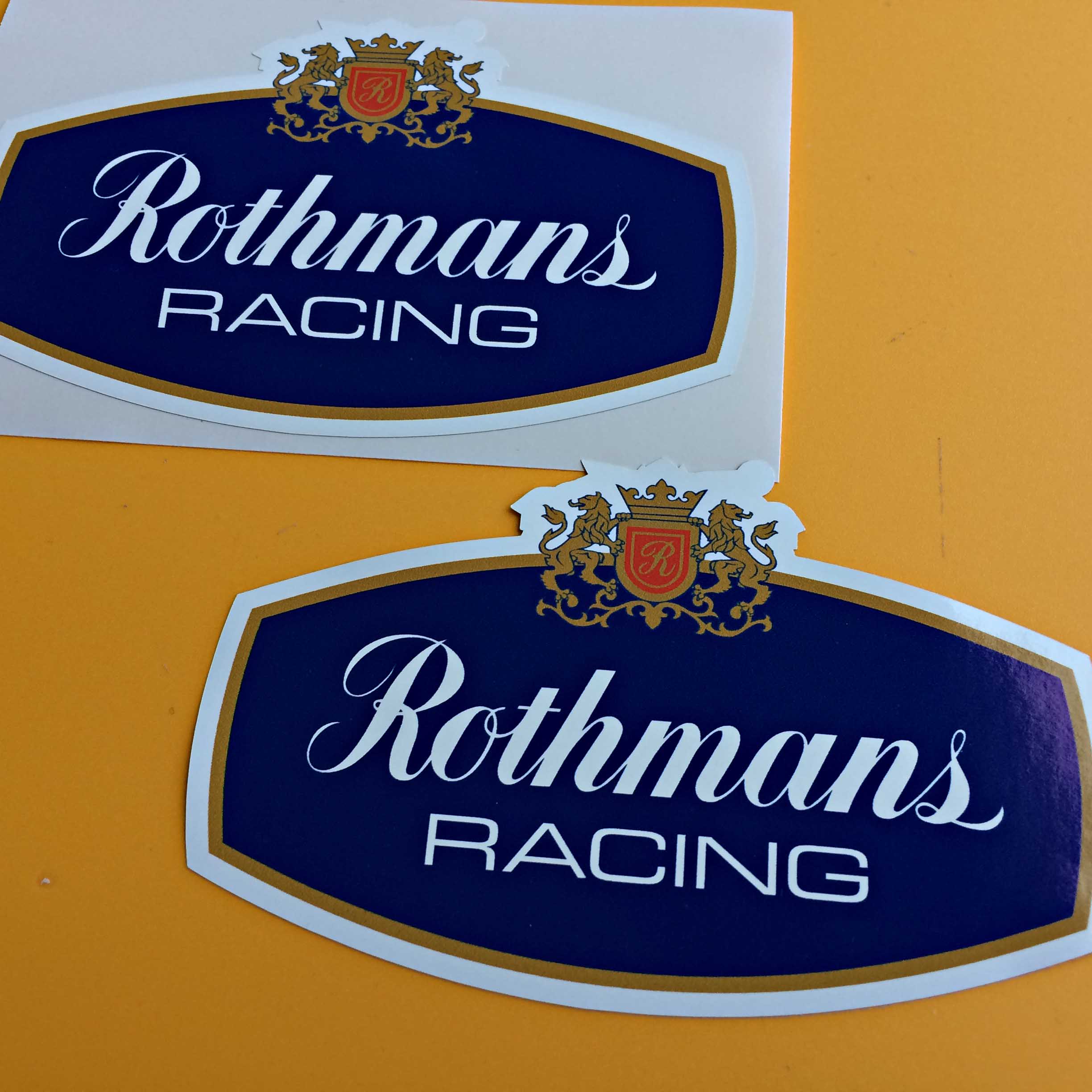 ROTHMANS RACING STICKERS. Rothmans Racing in white lettering on a blue background. Above are two golden lions either side of a gold crown and shield. The shield has a gold letter R on a red background.