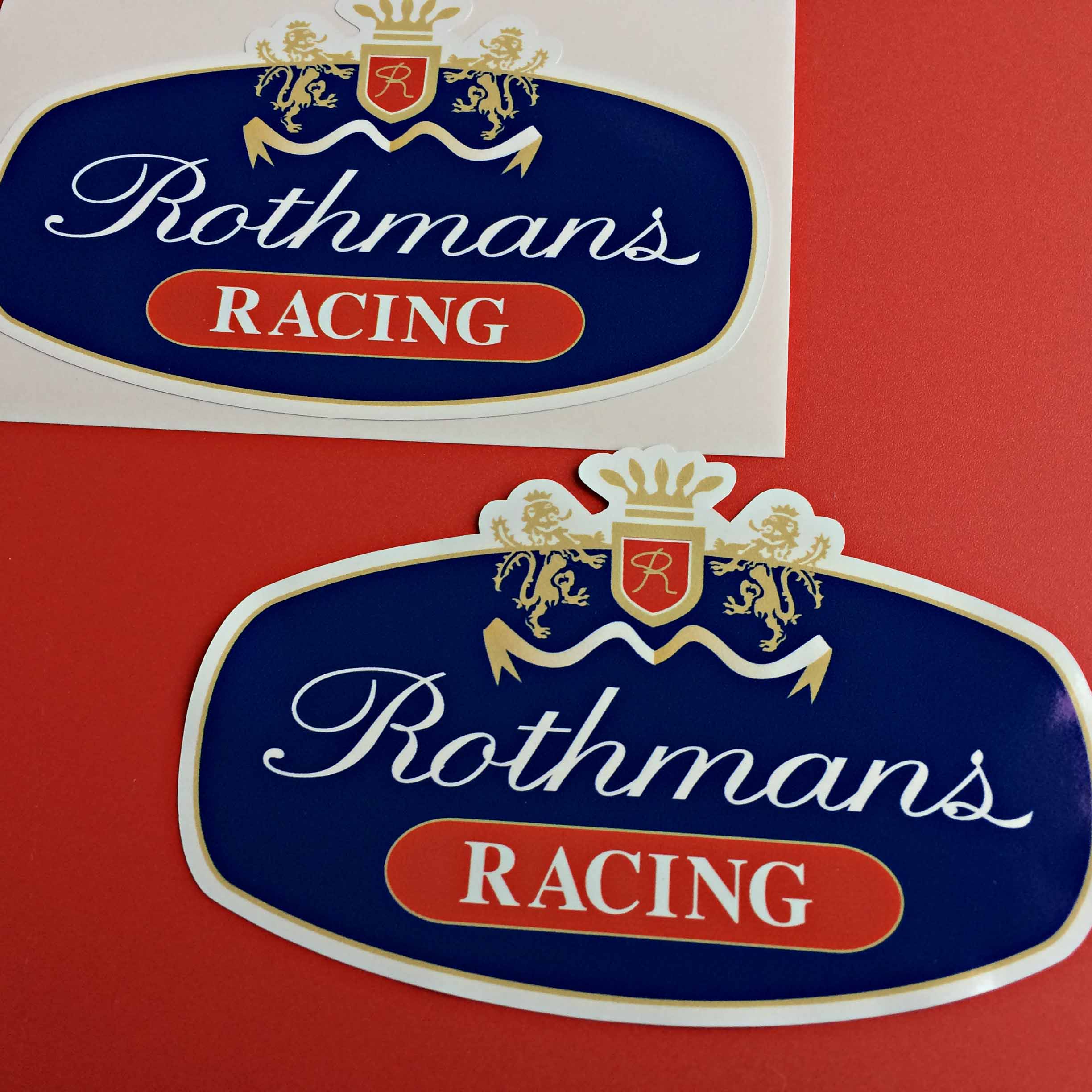 Rothmans Racing in white lettering on a blue and red background. Two golden lions are either side of a crown and shield. The shield has a gold letter R on a red background.