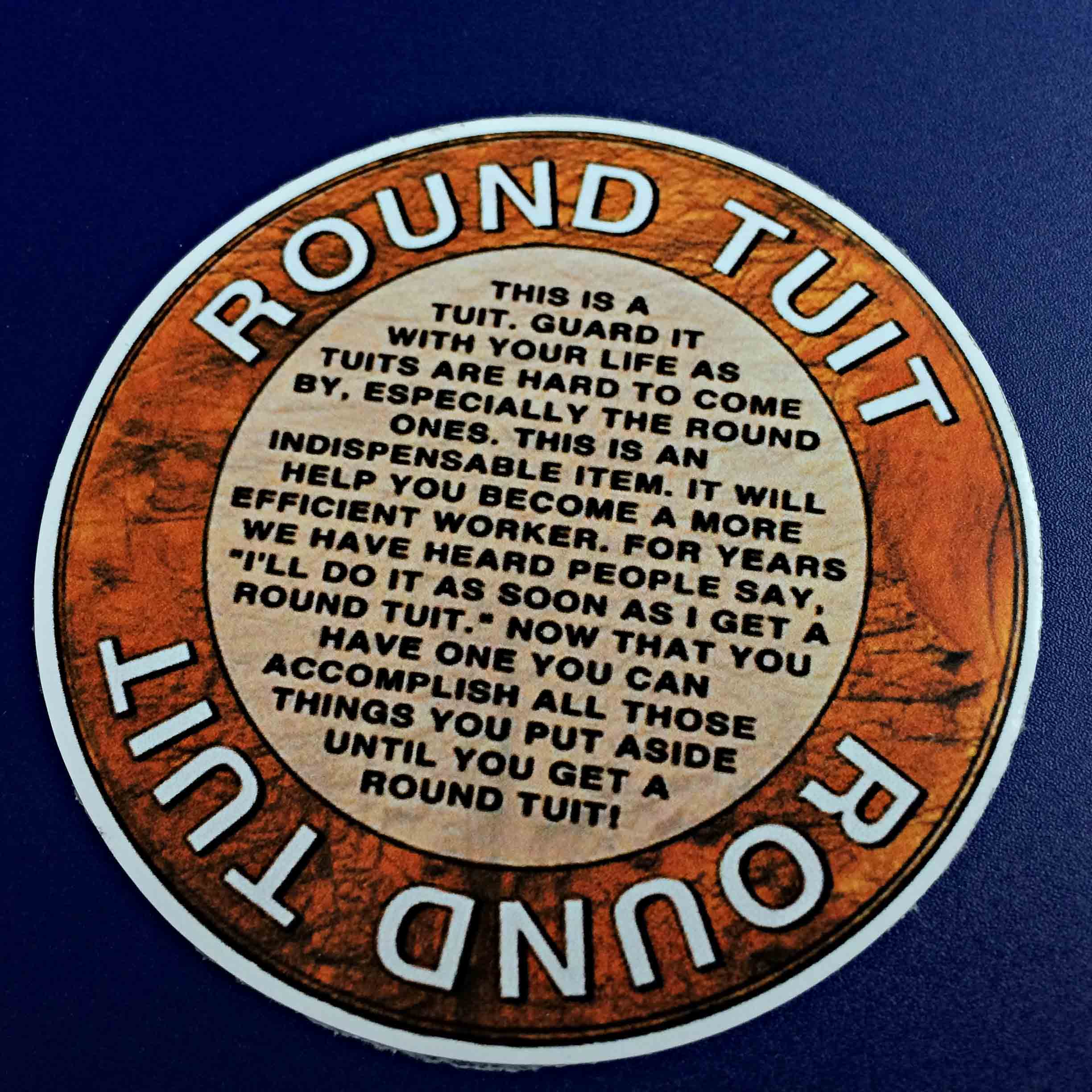 ROUND TUIT HUMOROUS STICKER. Round Tuit in white lettering on a brown outer circle. The inner circle contains the Round Tuit poem in black lettering.