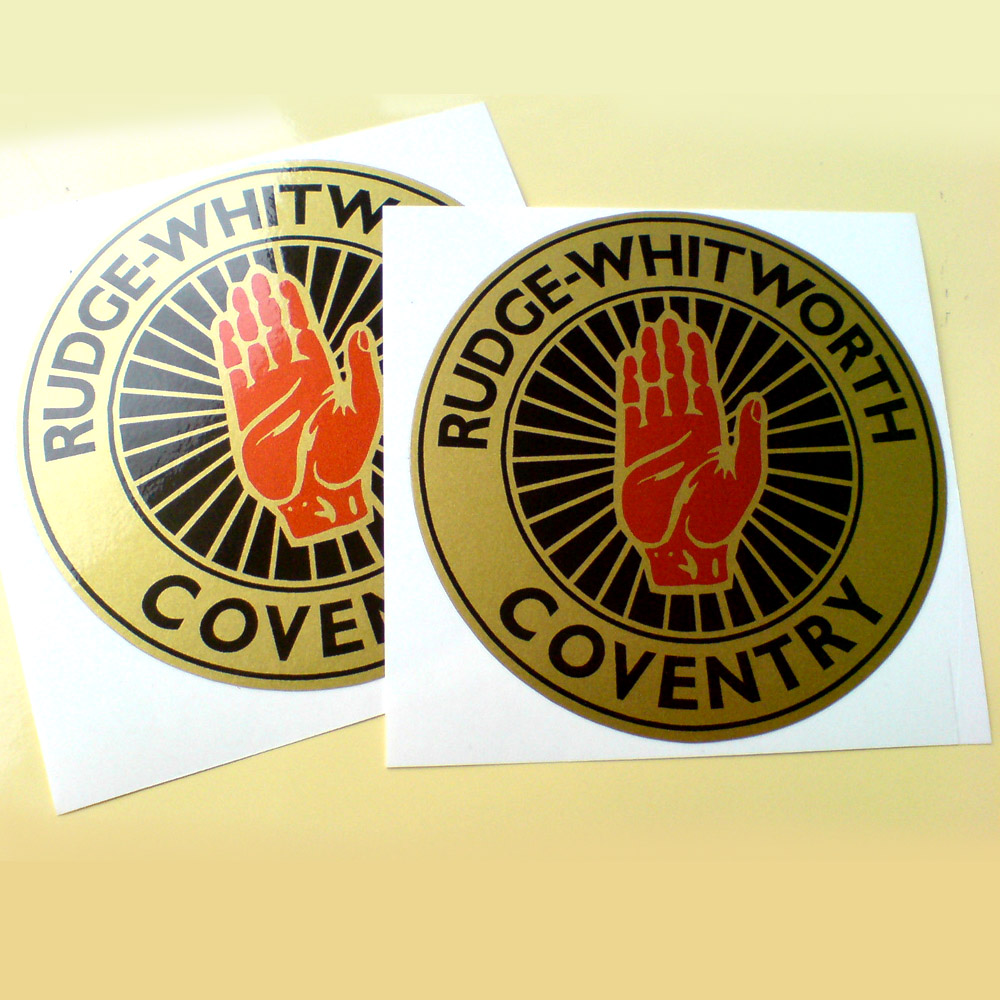 Rudge-Whitworth Coventry in black lettering on a gold outer circle. Centre is a red hand on a gold spoked wheel.