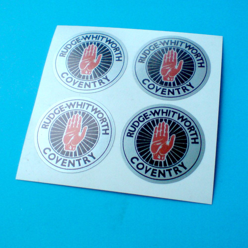RUDGE WHITWORTH WIRE WHEEL STICKERS. Rudge-Whitworth Coventry in black lettering on a silver outer circle. Centre is a red hand on a silver spoked wheel.