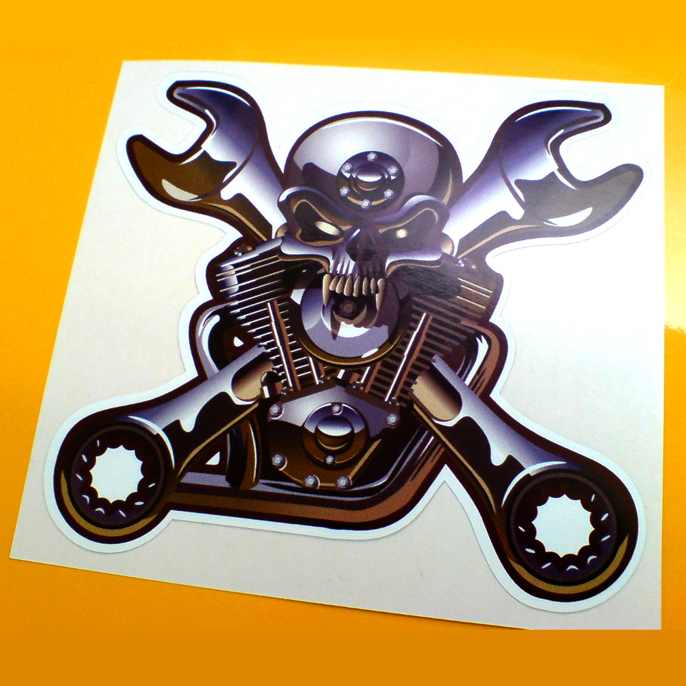 SKULL AND CROSSED SPANNERS STICKER. A chrome effect sticker. A skull overlays two crossed spanners. In the background is a motorbike engine.