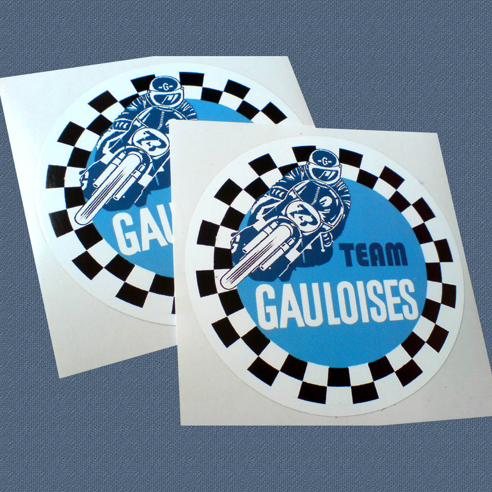 Two concentric circles. The outer circle is black and white chequer and the inner circle is pale blue. Team Gauloises lettering and a motorcyclist on his bike all in blue and white are in the centre.