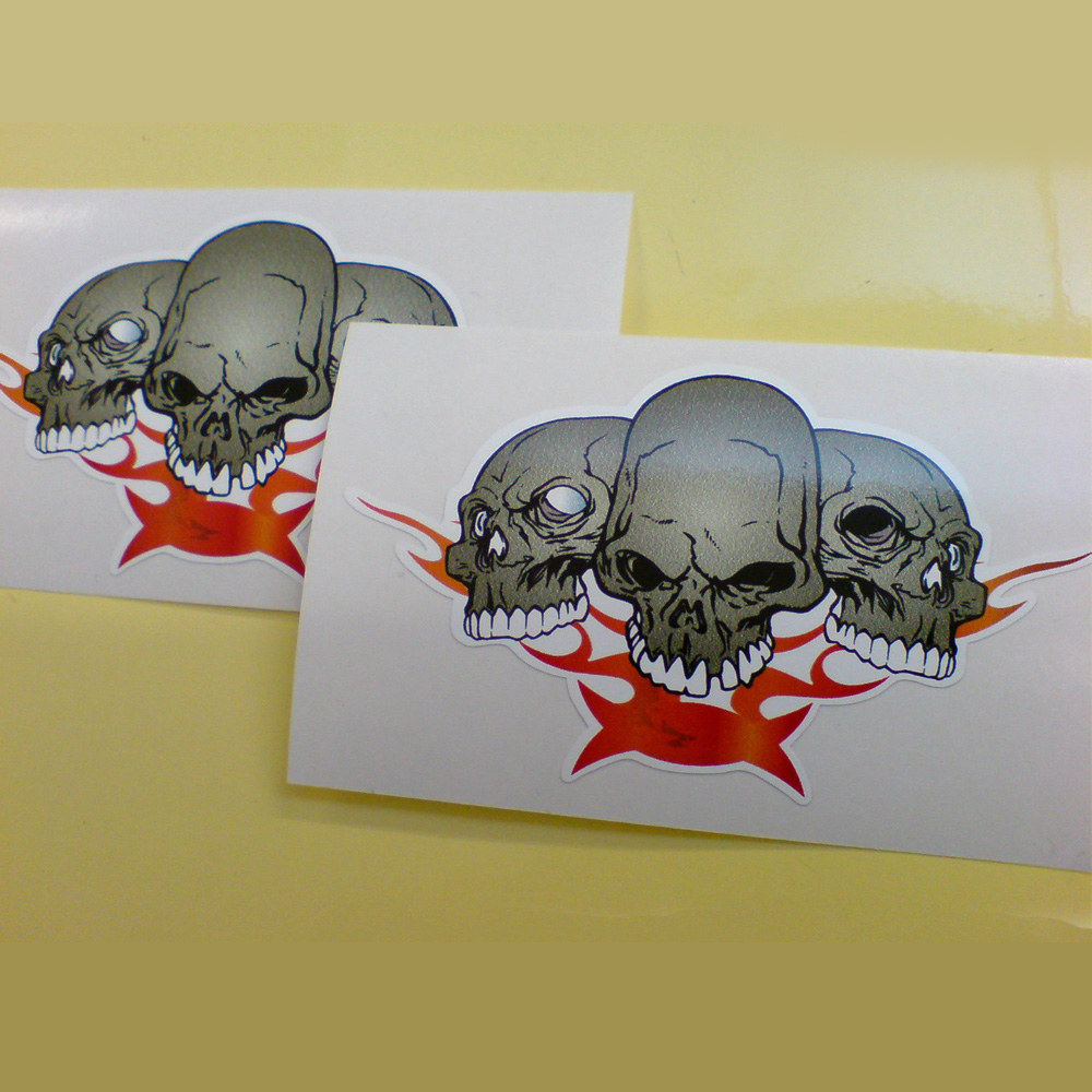THREE SKULLS STICKERS. A row of three grey skulls with white teeth. Red and orange flames are below.